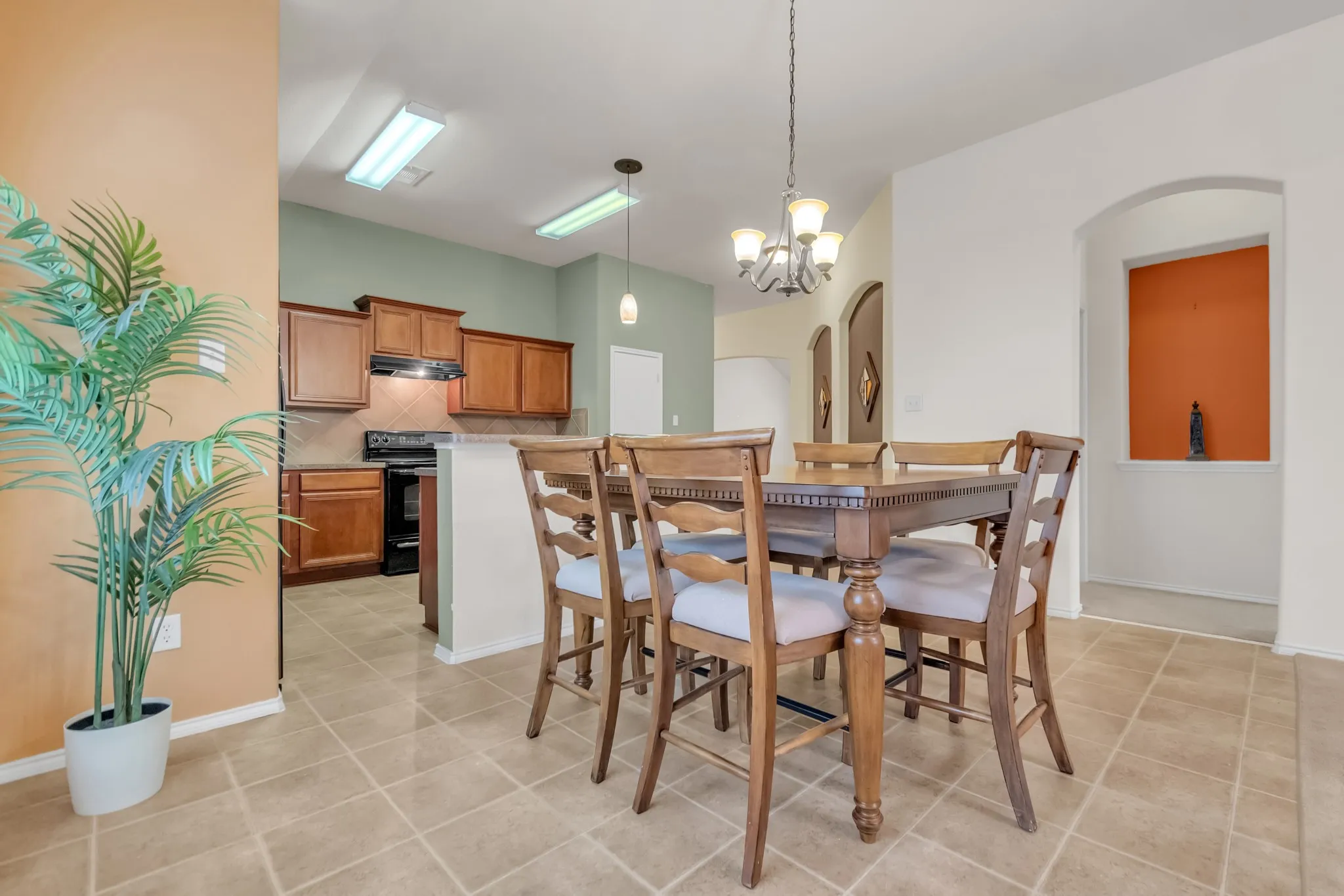 Tile flooring throughout, kitchen featuring wood cabinetry and black appliances, recessed wall niche, and arched doorways