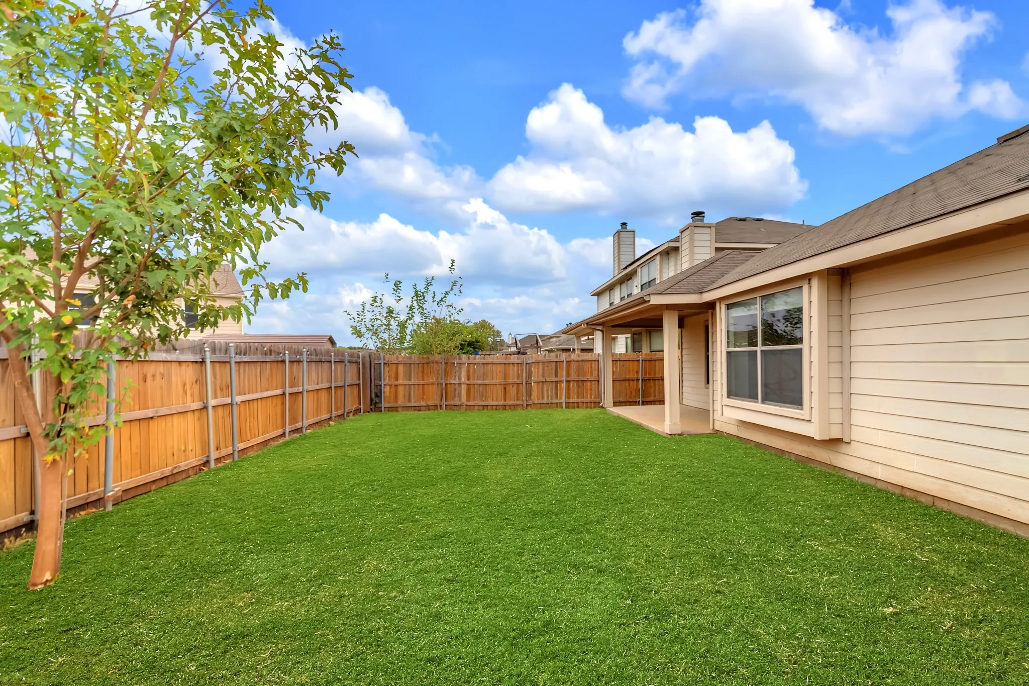 Expansive backyard featuring a manicured lawn, full wood fencing, and a covered patio area