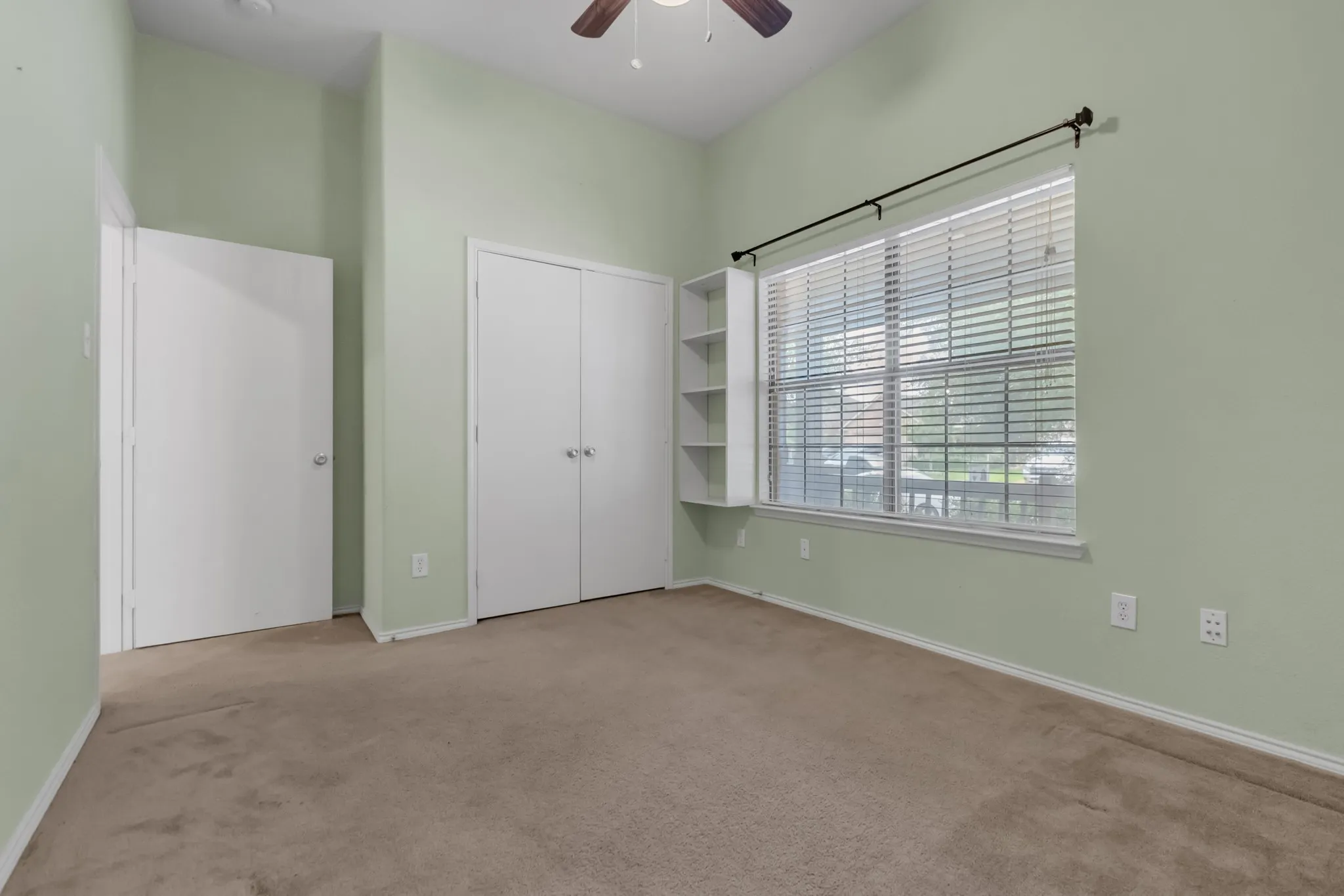 Vaulted ceiling with ceiling fan, large window with blinds, built-in shelving, and two closet doors
