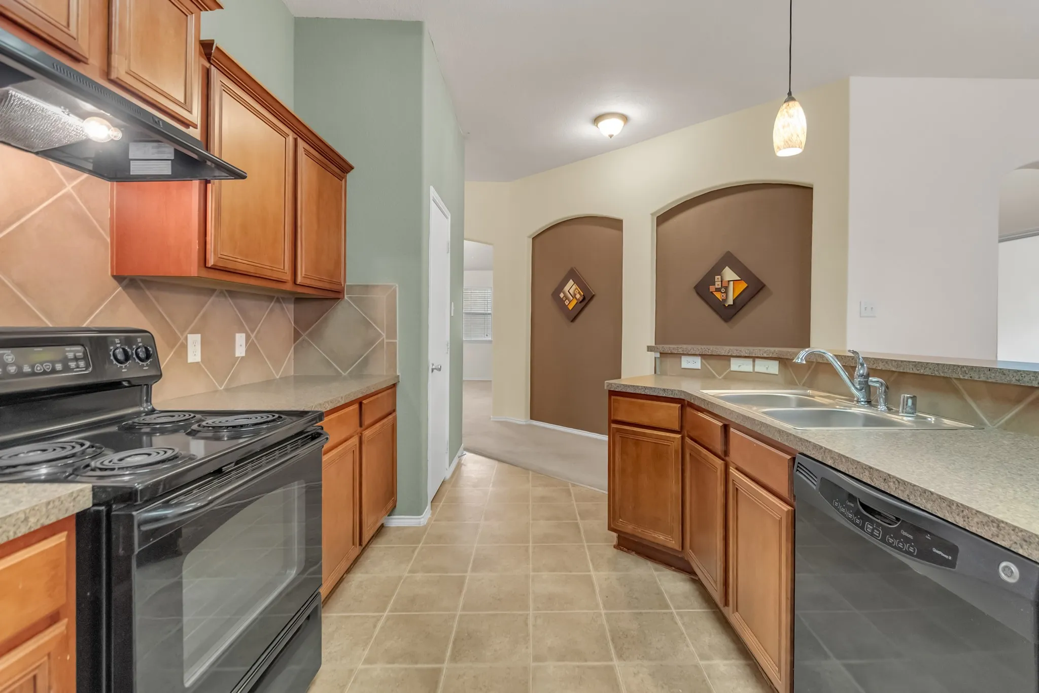 Tile flooring, wood cabinetry, built-in range, dual basin sink, and built-in dishwasher