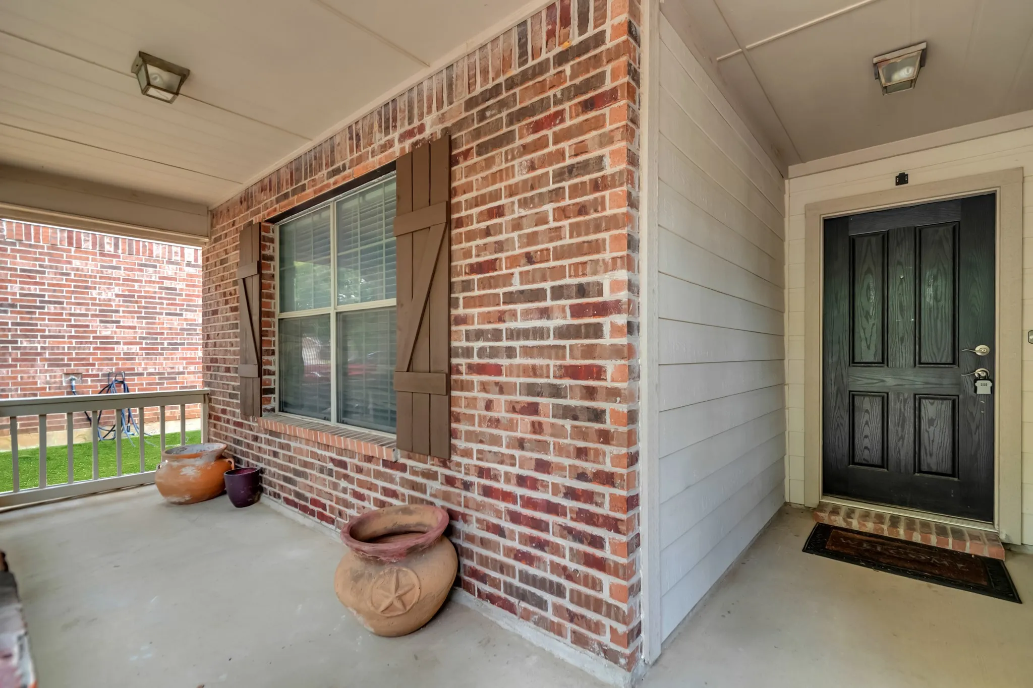 Covered front porch with red brick exterior, large multi-pane window, and black six-panel entry door with sidelights