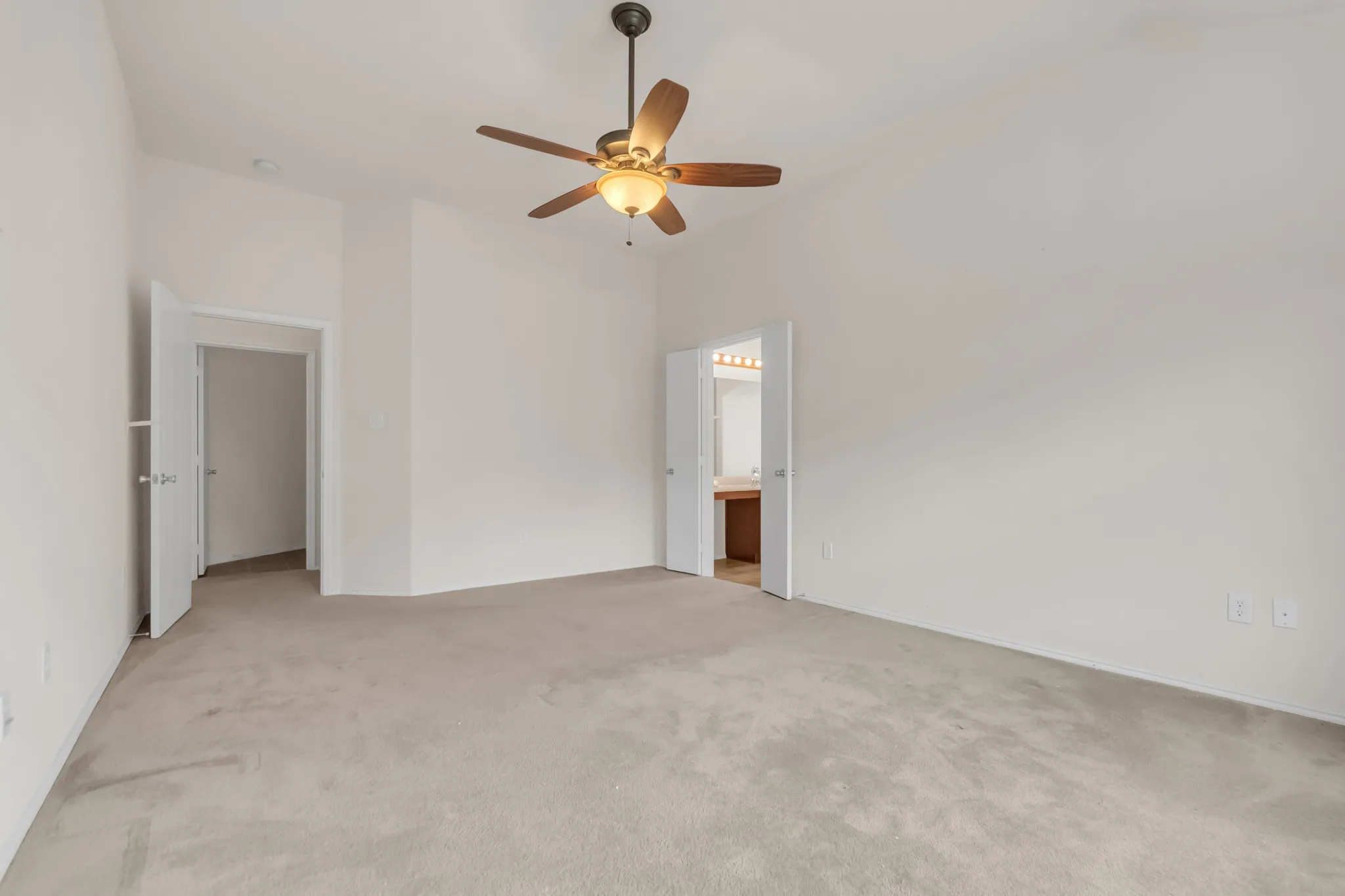 Vaulted ceilings with a ceiling fan, light-toned carpeting, and a door leading to a bathroom with a wood-finish vanity