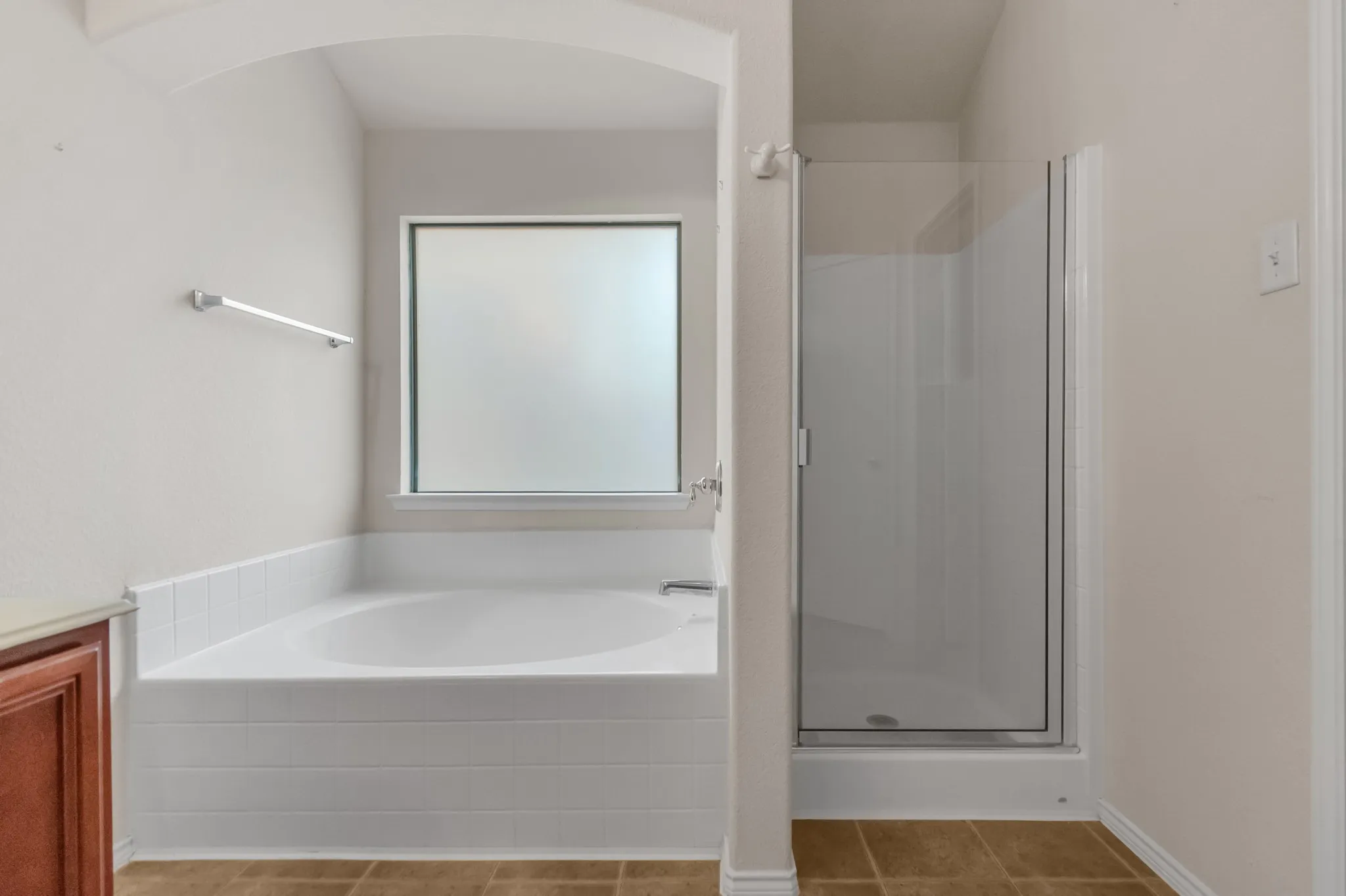 White tiled soaking tub with a frosted window and an adjacent glass-enclosed shower stall