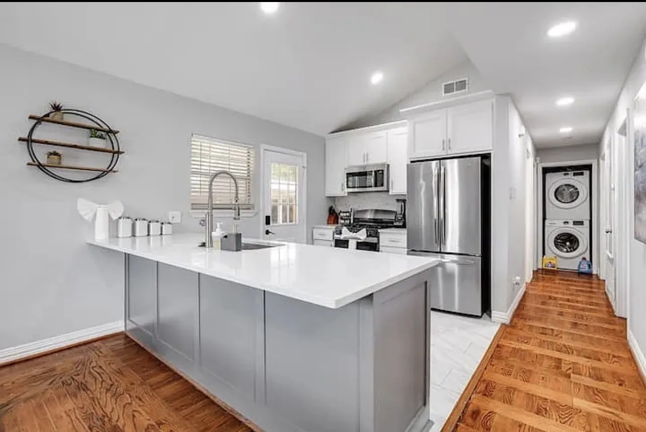 Bright kitchen featuring a central island with a sink, white cabinetry, stainless steel appliances, and a stacked washer and dryer