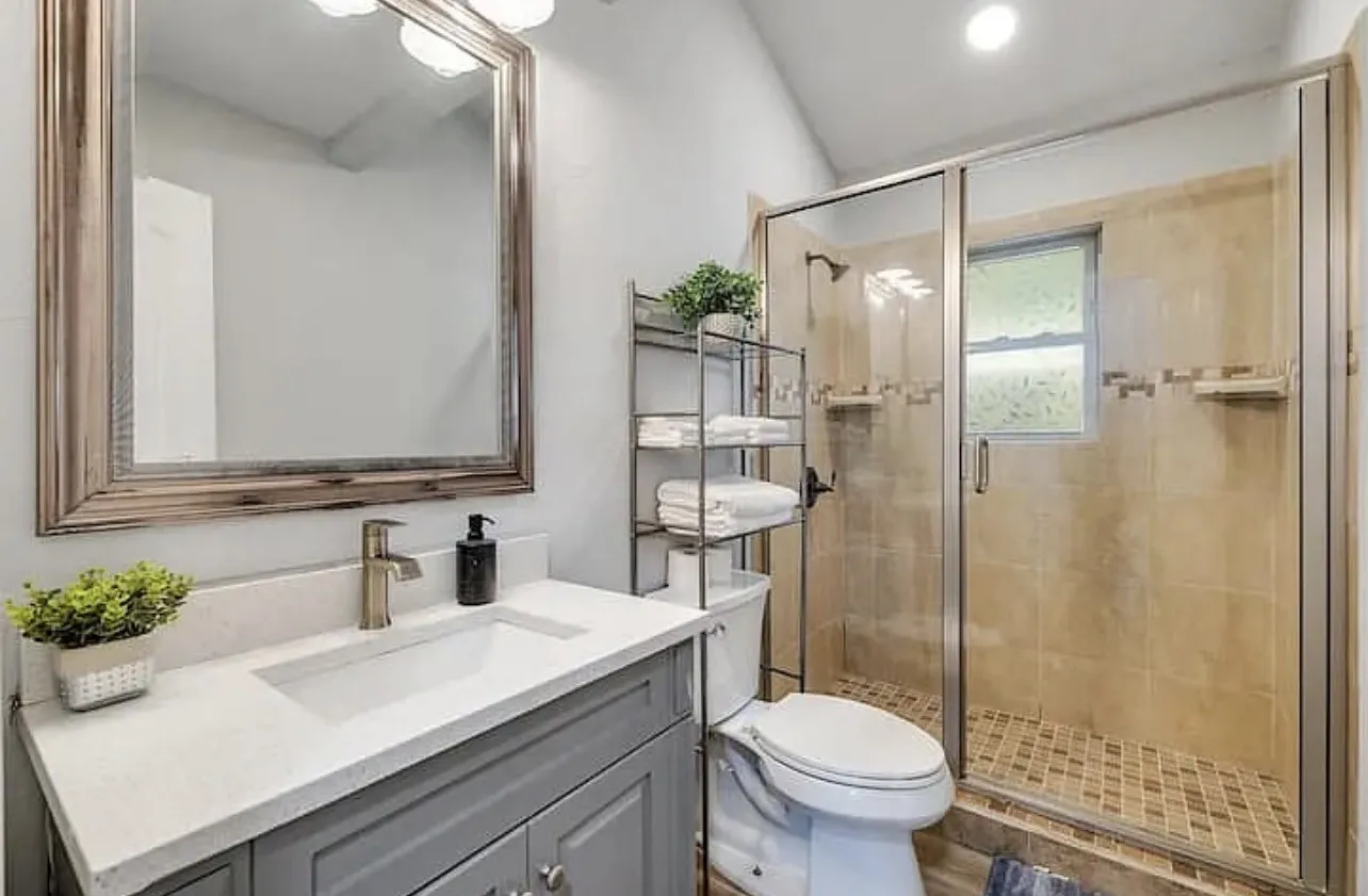 Vanity with white countertop and integrated sink, brushed nickel faucet, large framed mirror, and glass-enclosed shower with tiled walls and floor