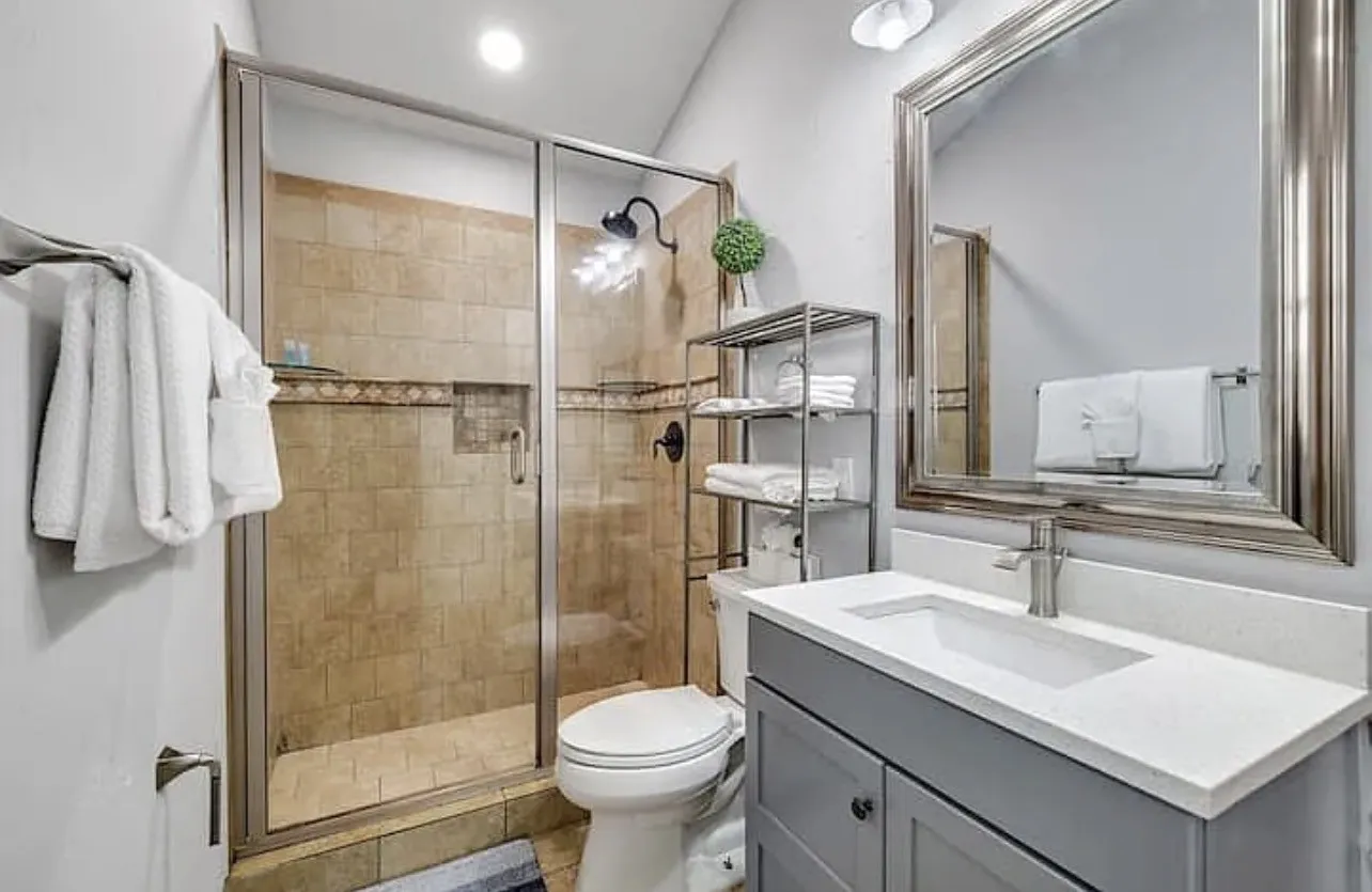 Shower with tile surround and glass enclosure, modern vanity with white countertop, chrome faucet, and framed mirror