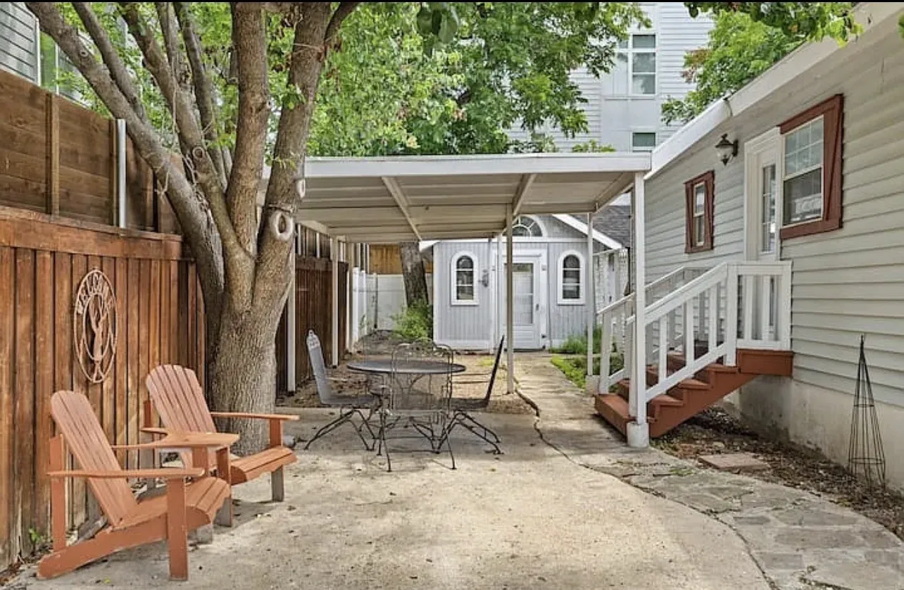 Paved patio area featuring a mature tree, wood fencing, and a covered walkway