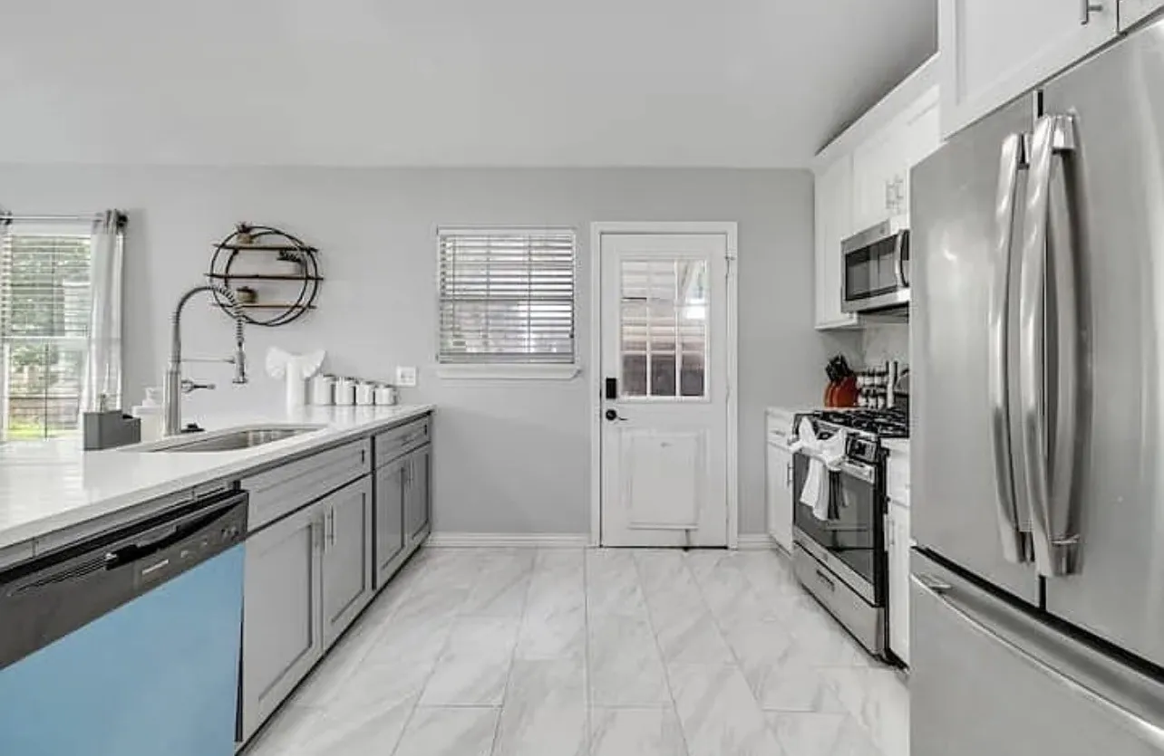 Kitchen featuring stainless steel appliances, light-toned cabinetry, light countertops, a built-in sink, and tile flooring