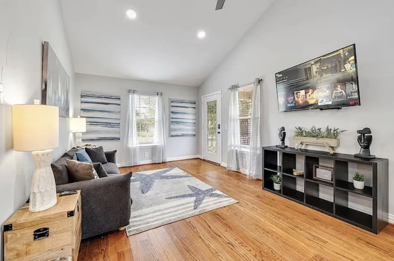 Vaulted ceiling with recessed lighting, wood-finish flooring, two windows with white curtains, and a glass-paneled door