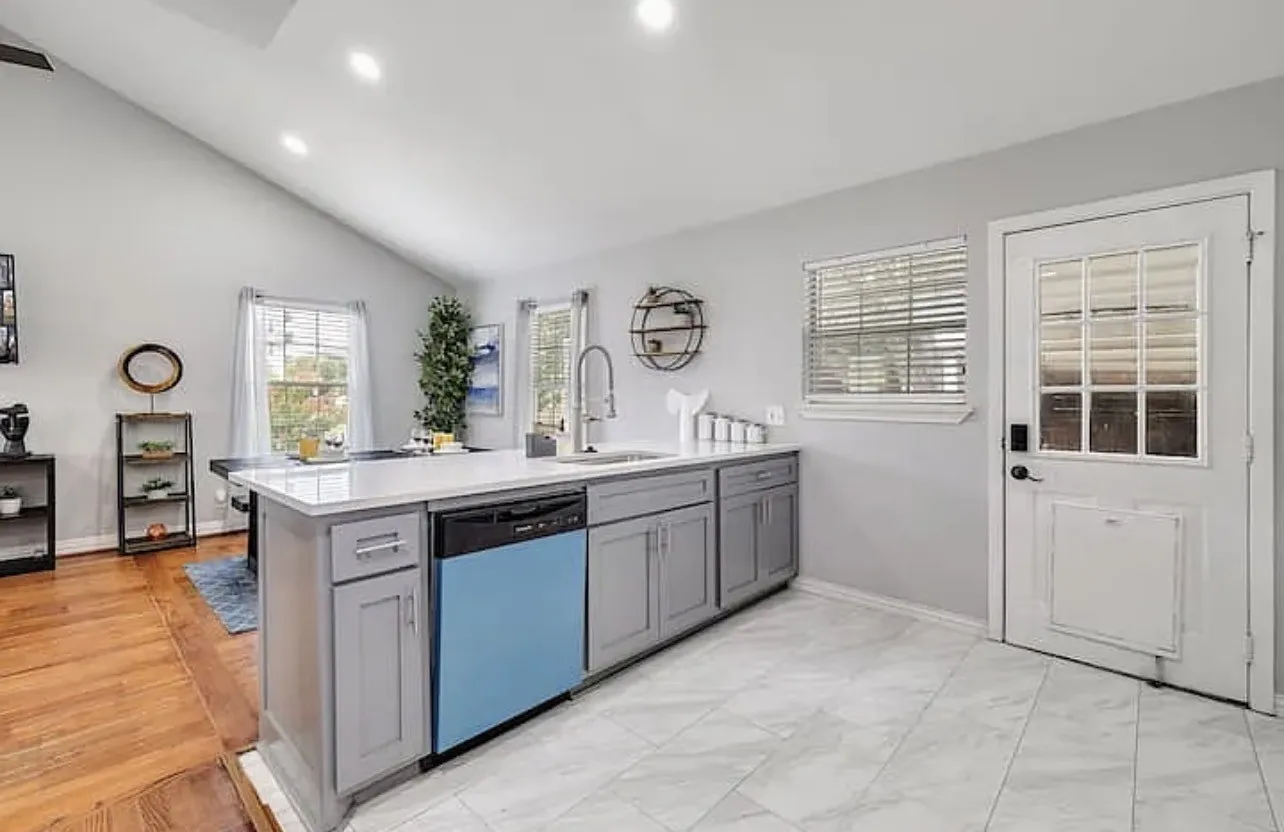 Vaulted ceiling with recessed lighting, kitchen island with sink and light gray cabinetry, white countertops, tile flooring, and a glass-paneled exterior door