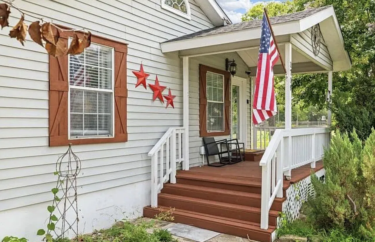 Inviting front porch with white railings, brown wood-finish steps, and a matching front door frame