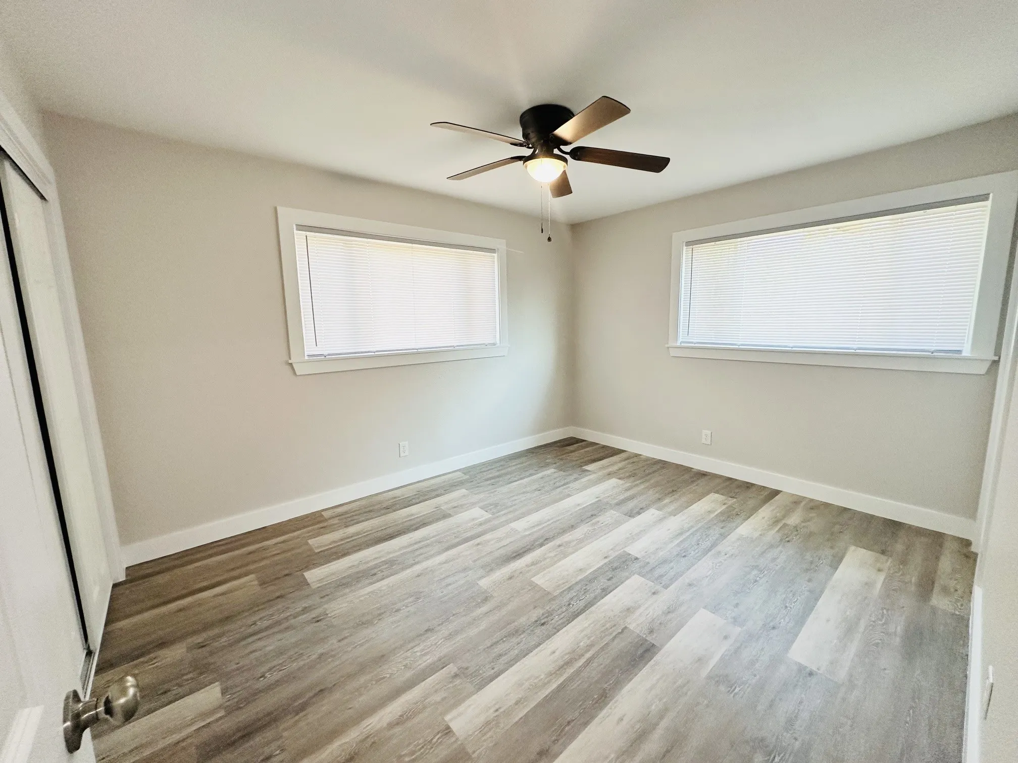 Room with wood-finish flooring, two large windows, and a ceiling fan with integrated lighting