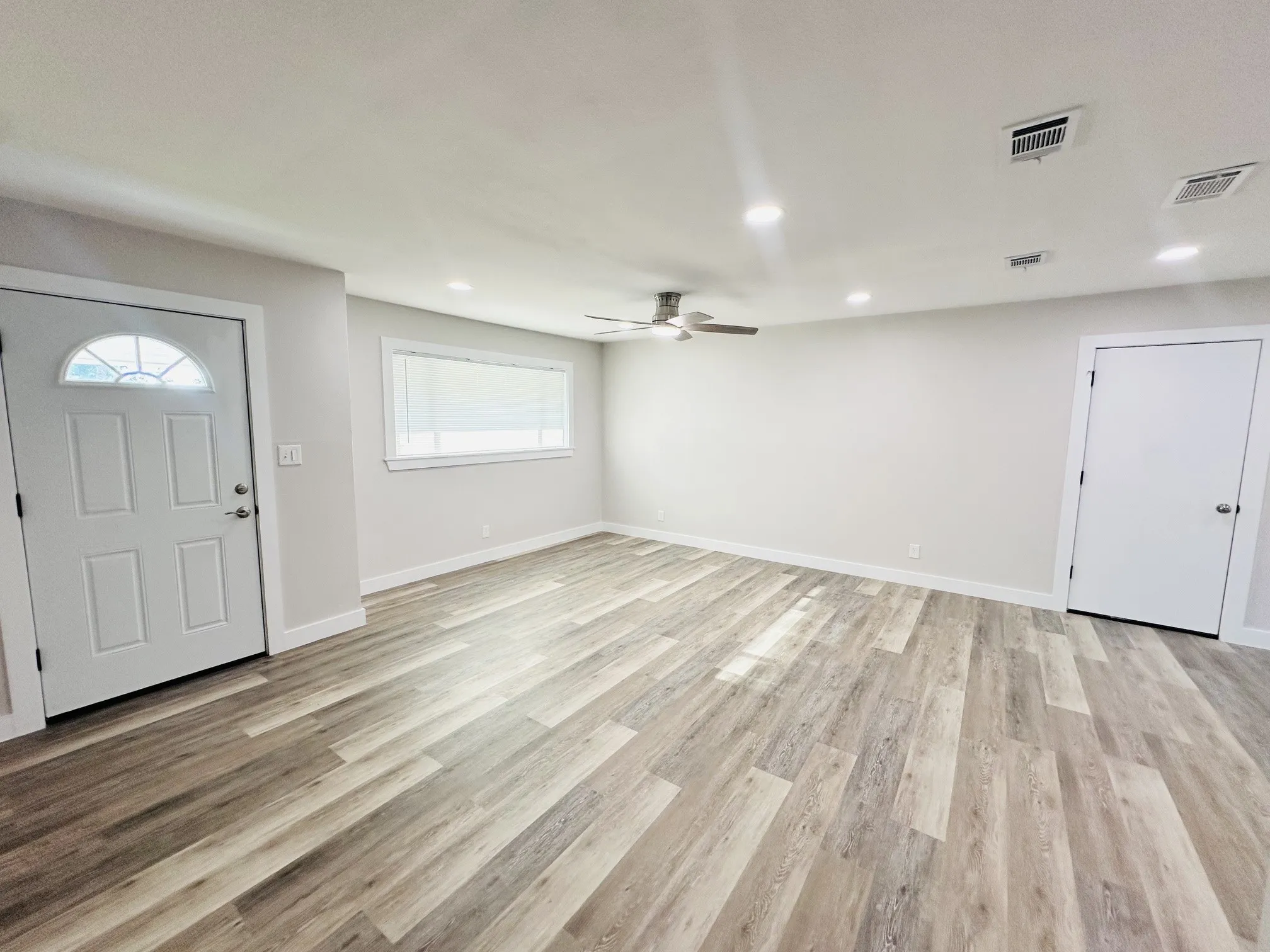 Wood-finish flooring throughout, recessed lighting, ceiling fan, white paneled door, and a horizontal window