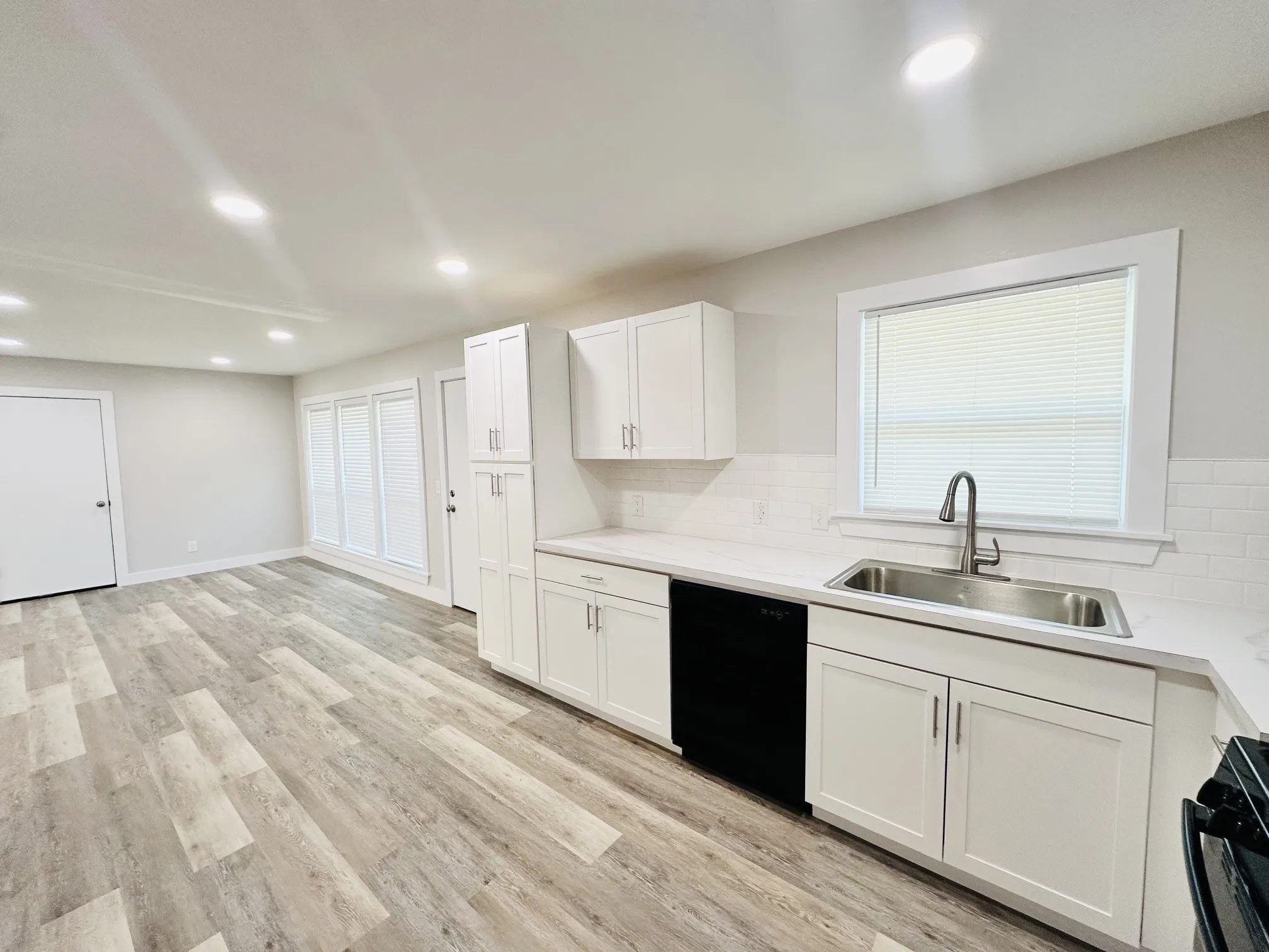 Light-toned wood-finish flooring, white shaker cabinetry, stainless steel sink, white subway tile backsplash, and recessed lighting