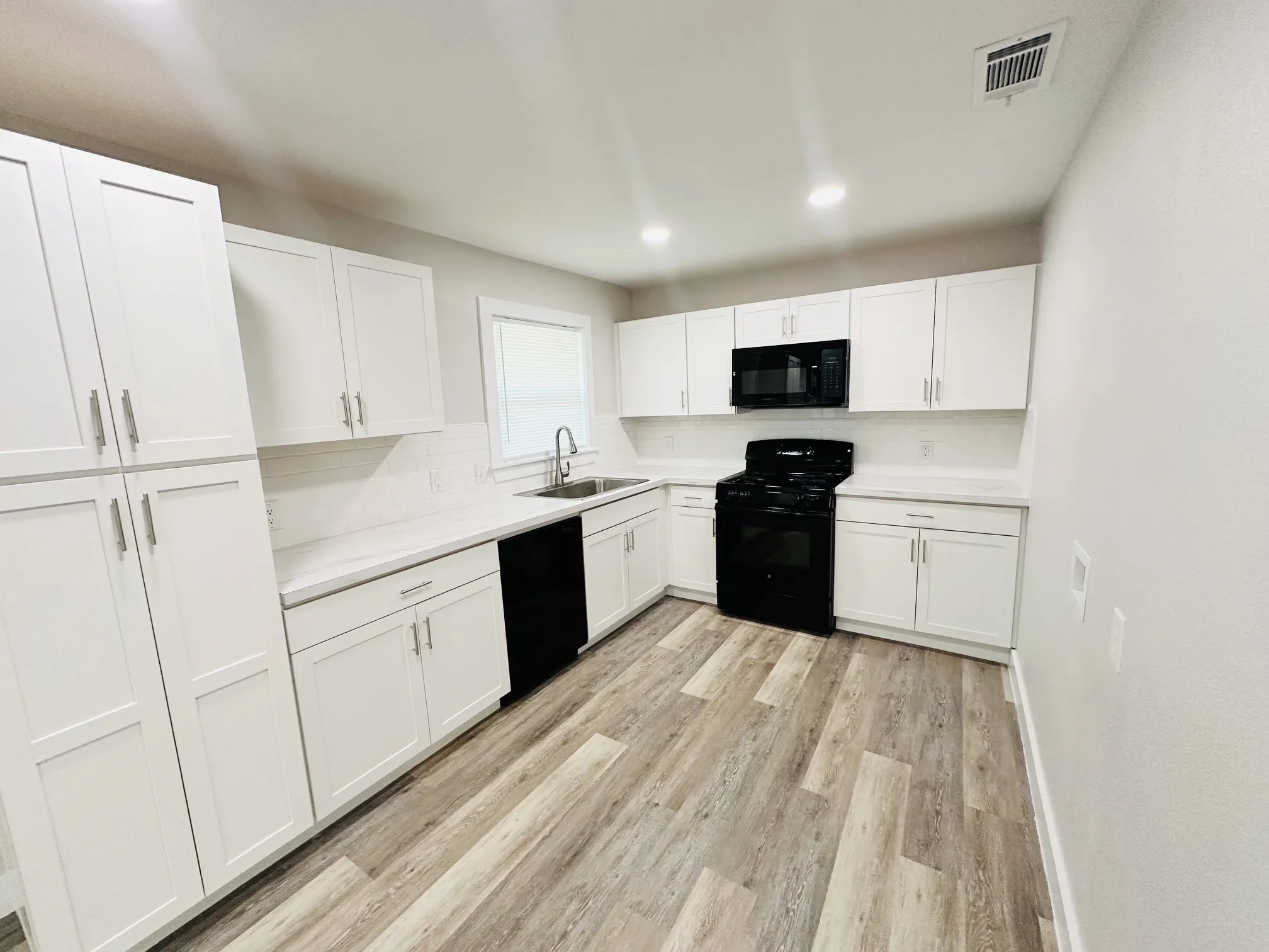 White shaker cabinetry, light-toned wood-finish flooring, white subway tile backsplash, recessed lighting, and stainless steel sink