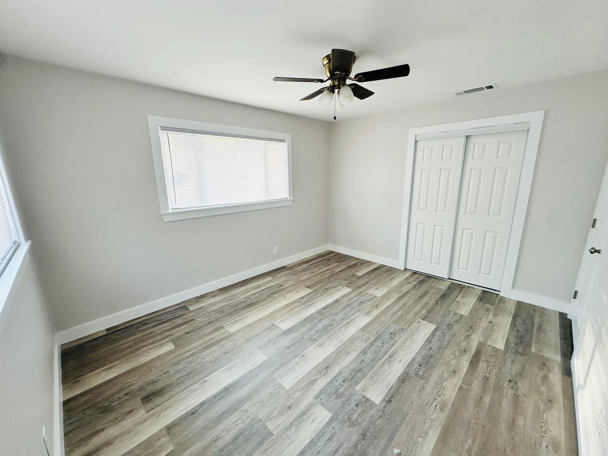Wood-finish flooring, ceiling fan with integrated lighting, sliding bi-fold closet doors, and window with horizontal blinds