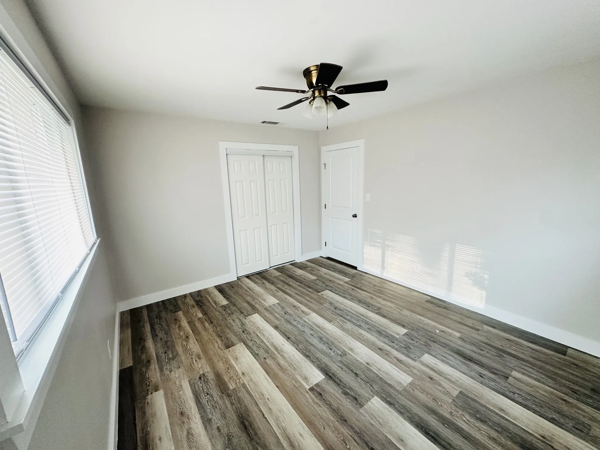Wood-finish flooring, ceiling fan, window with blinds, and white bi-fold closet doors