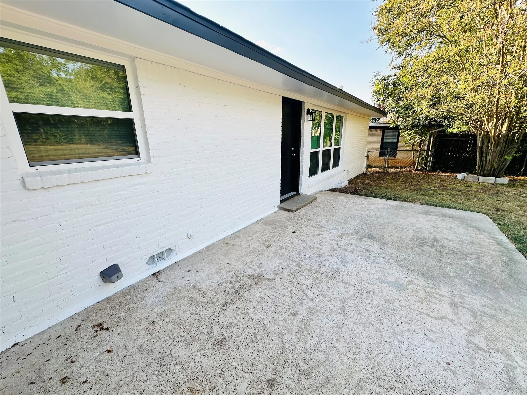 White-painted brick exterior, concrete patio, black soffit and fascia, white-framed windows, exterior lighting fixture