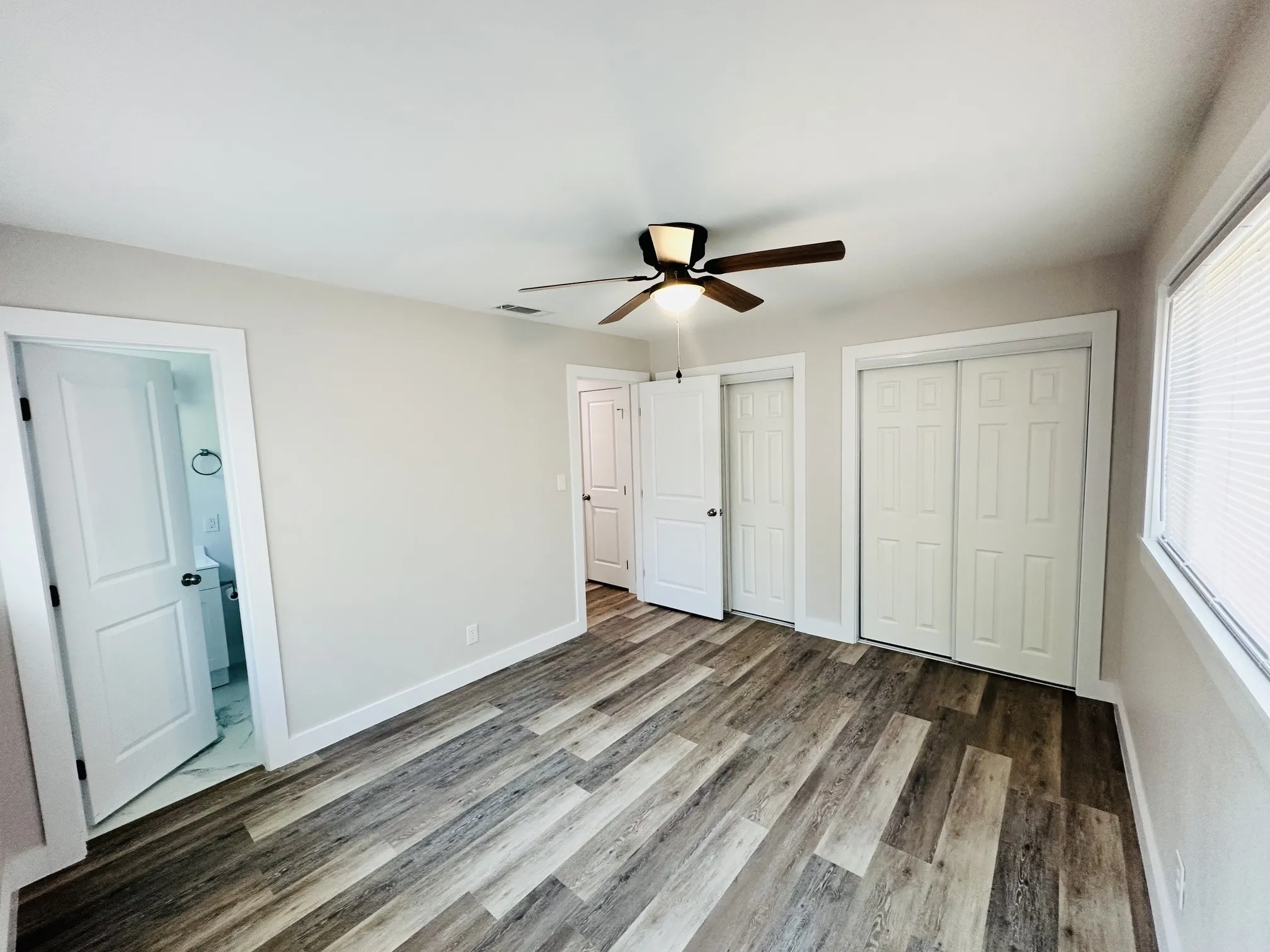 Wood-finish flooring throughout, white paneled doors, and a ceiling fan with integrated lighting