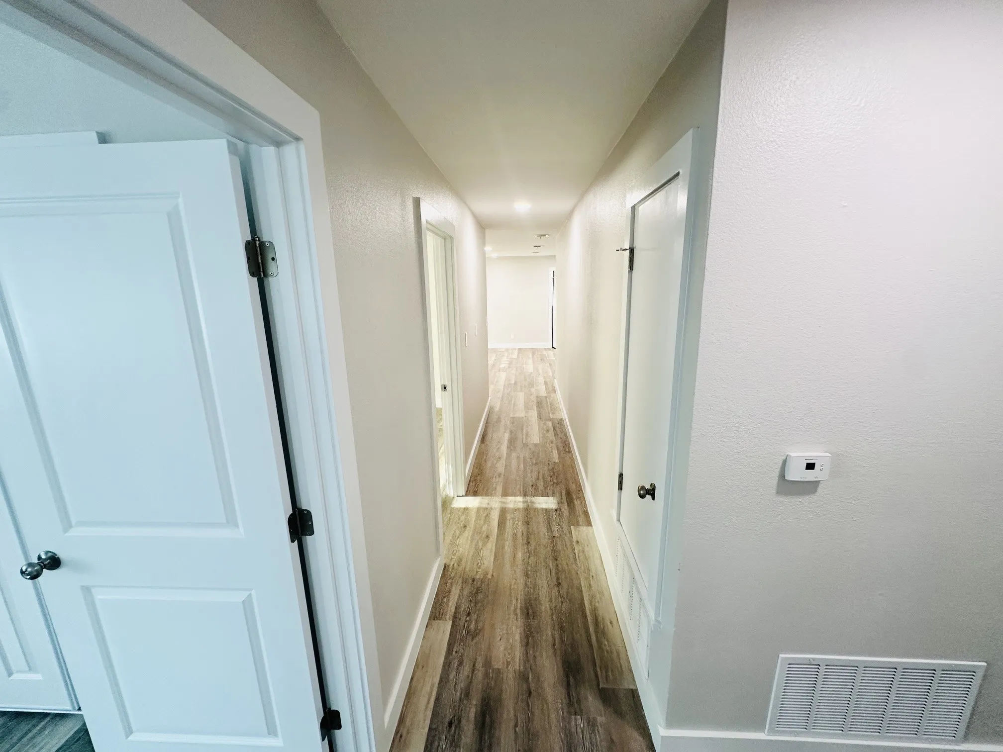 Hallway with wood-finish flooring, white paneled doors, and light-toned wall finishes