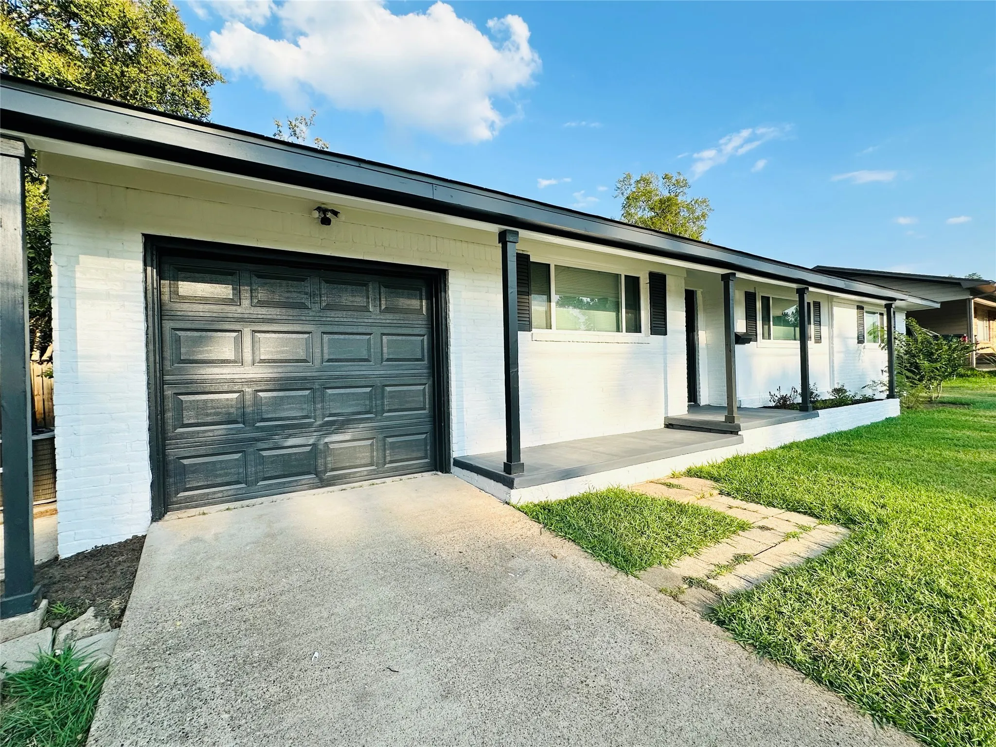 White brick exterior with black trim, an attached garage, a covered front porch, and a concrete driveway
