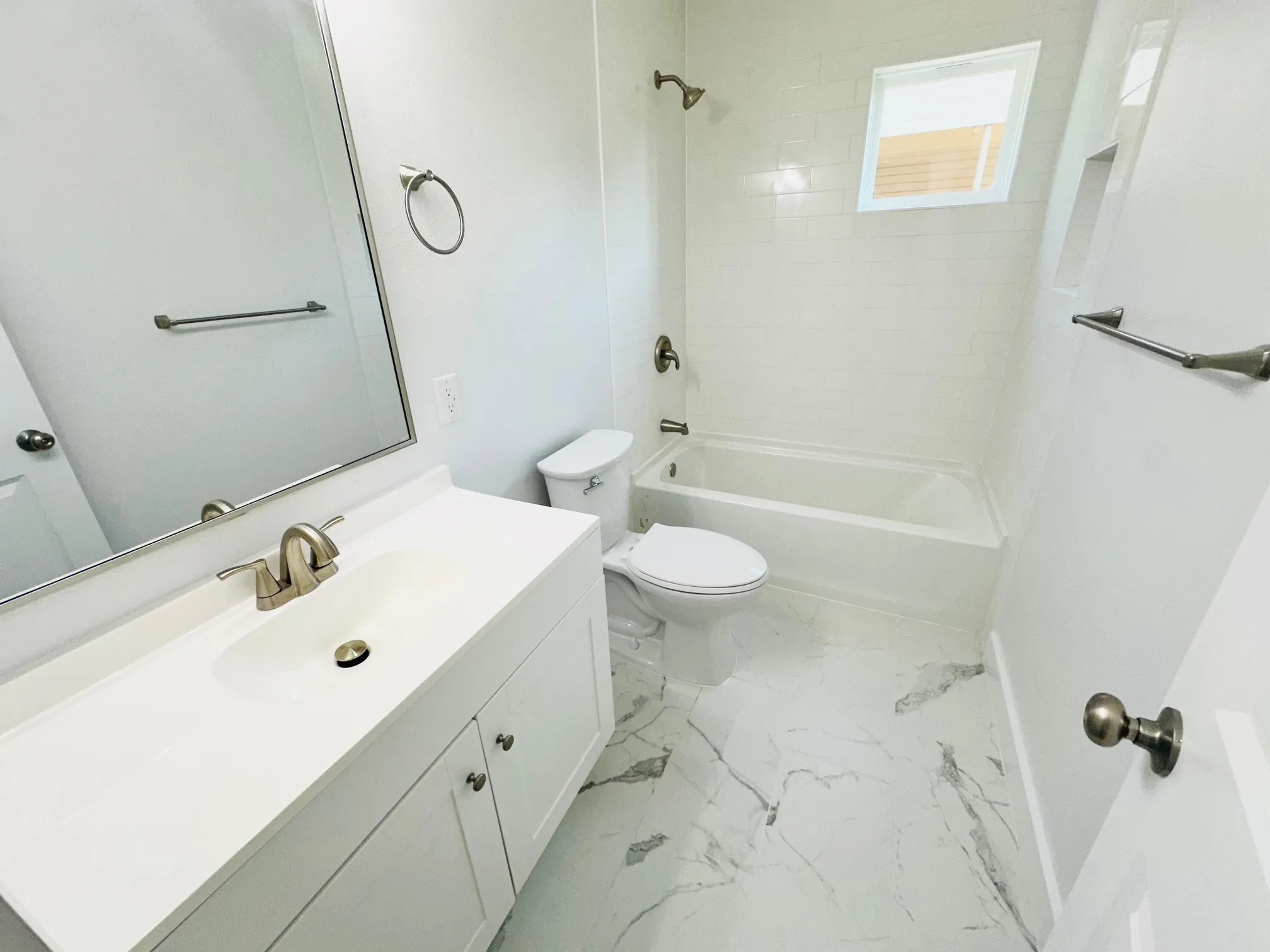 Bathroom featuring a white vanity with integrated sink, brushed nickel fixtures, a framed mirror, a bathtub with subway tile surround, and marble-look floor tiles