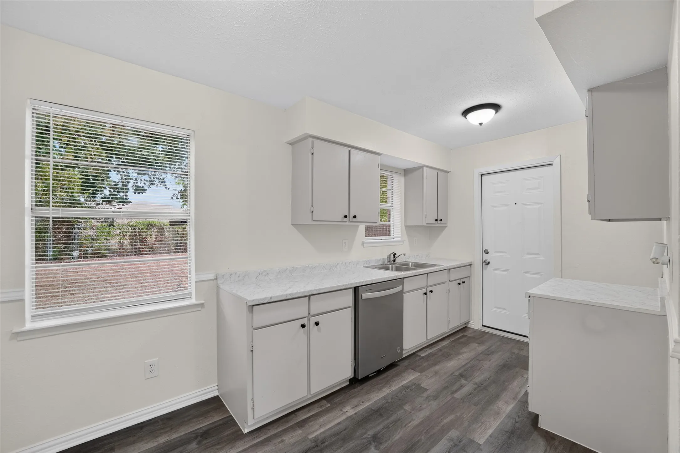 Kitchen featuring wood-finish flooring, white cabinetry, a stainless steel dishwasher, and light-toned countertops