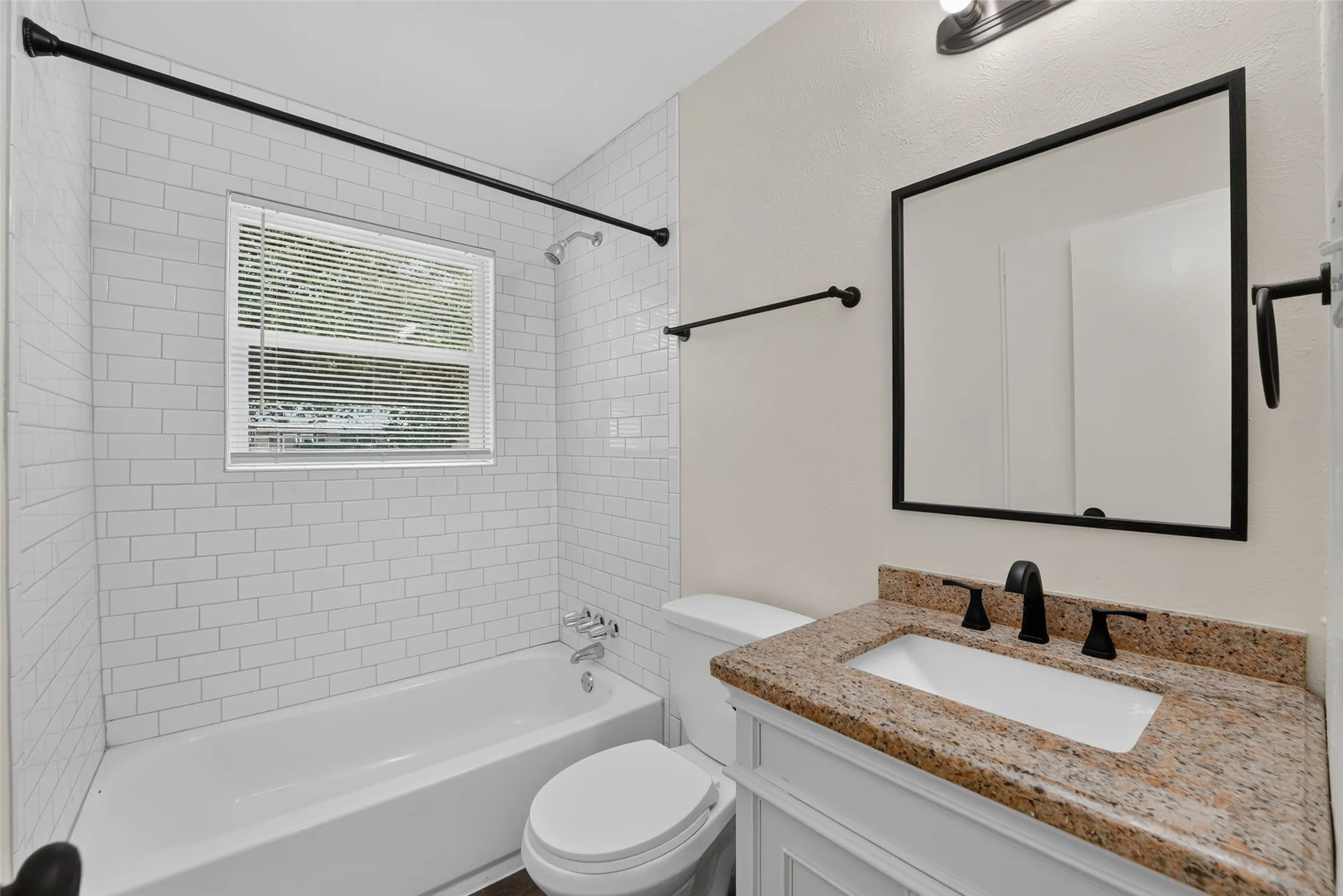 Bathroom featuring a white subway tile shower, white bathtub, vanity with stone countertop, and matte black fixtures
