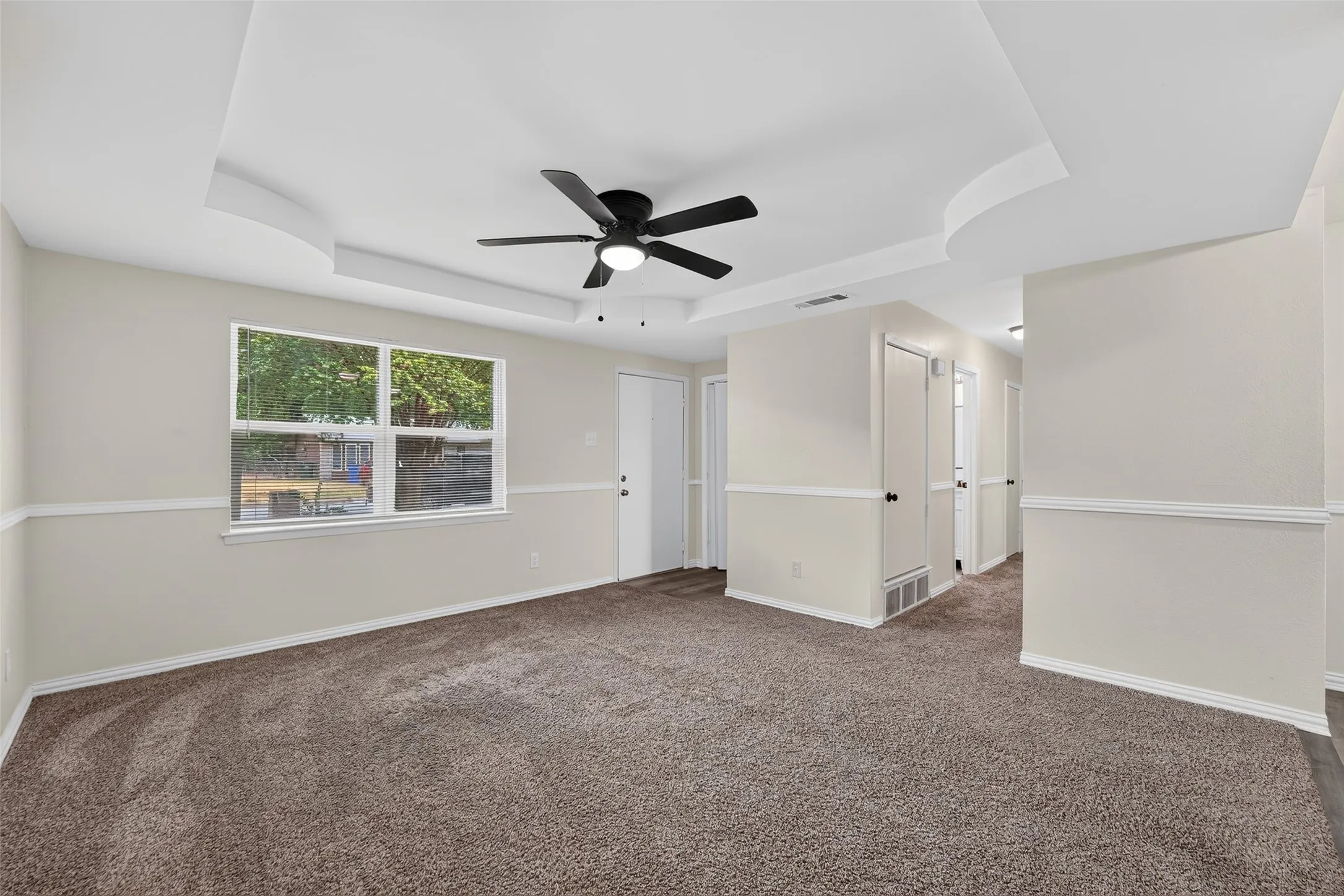 Tray ceiling with recessed lighting and a ceiling fan, neutral carpet flooring, and a large window