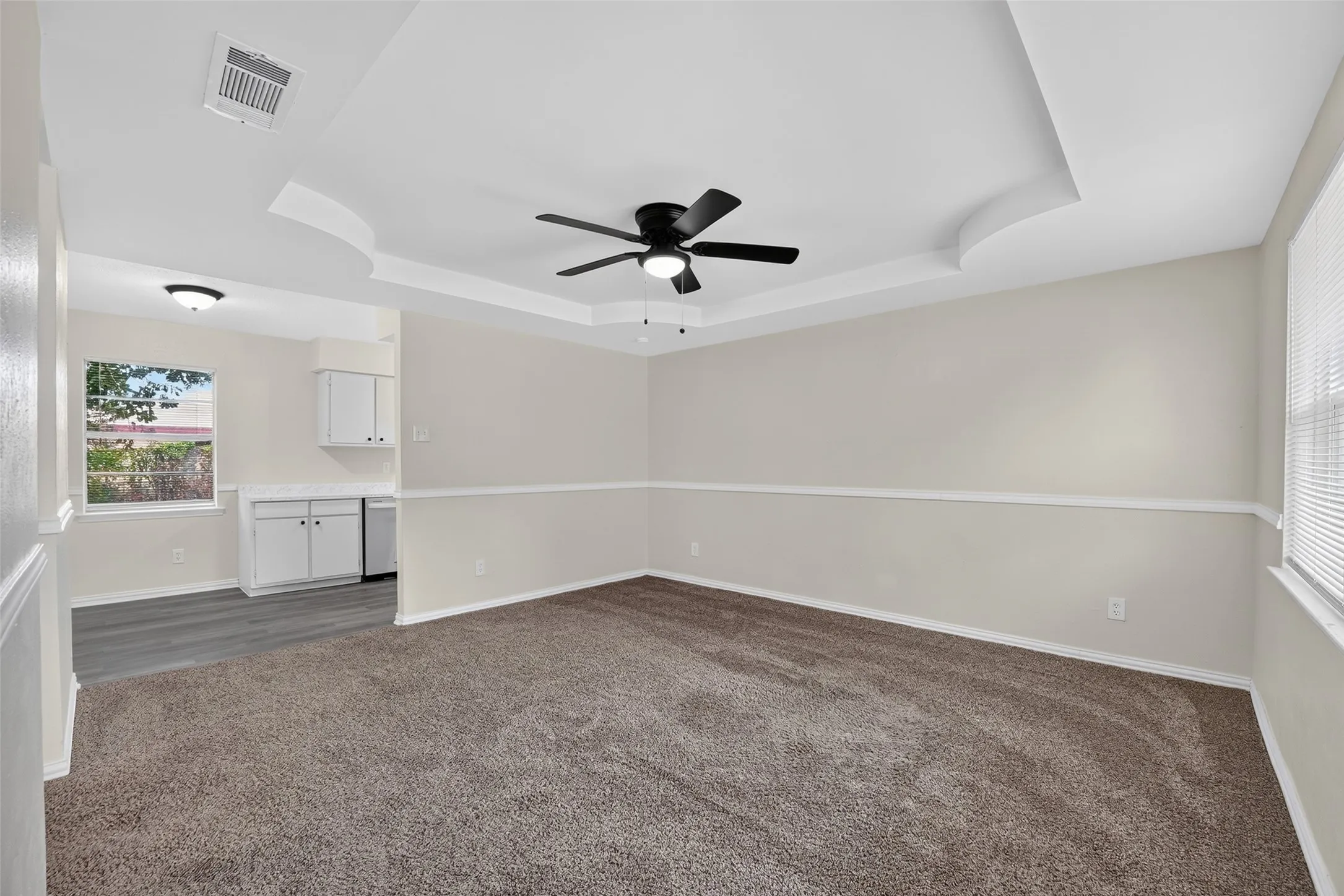 Tray ceiling with a ceiling fan, neutral carpet, picture rail molding, and a built-in cabinet with a countertop