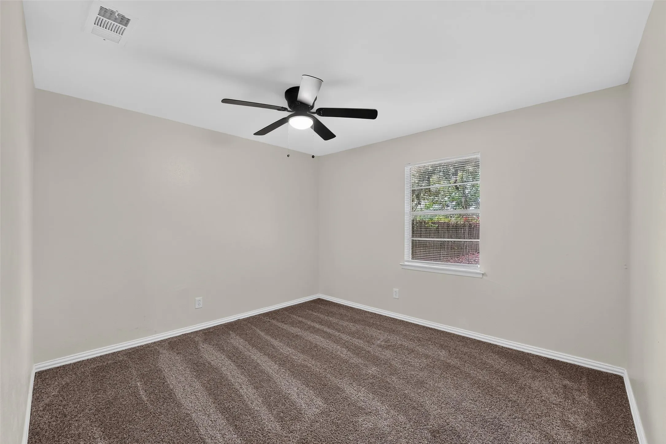 Neutral wall color, dark brown carpeting, and a ceiling-mounted fan with integrated lighting