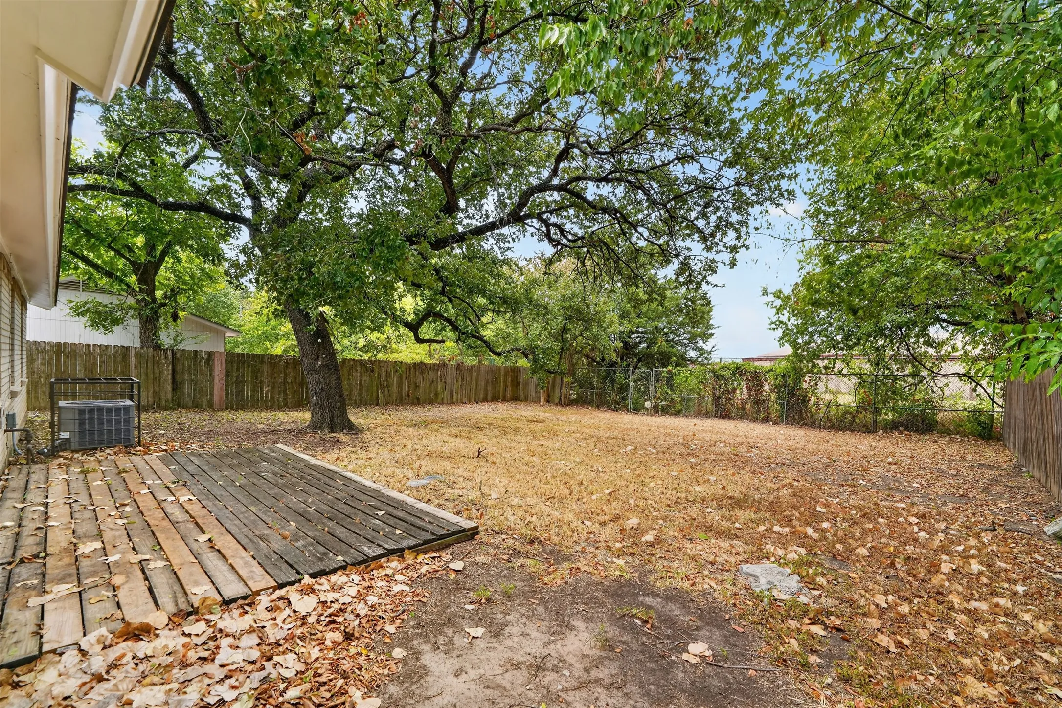 Expansive backyard featuring a wood deck, mature trees, and privacy fencing