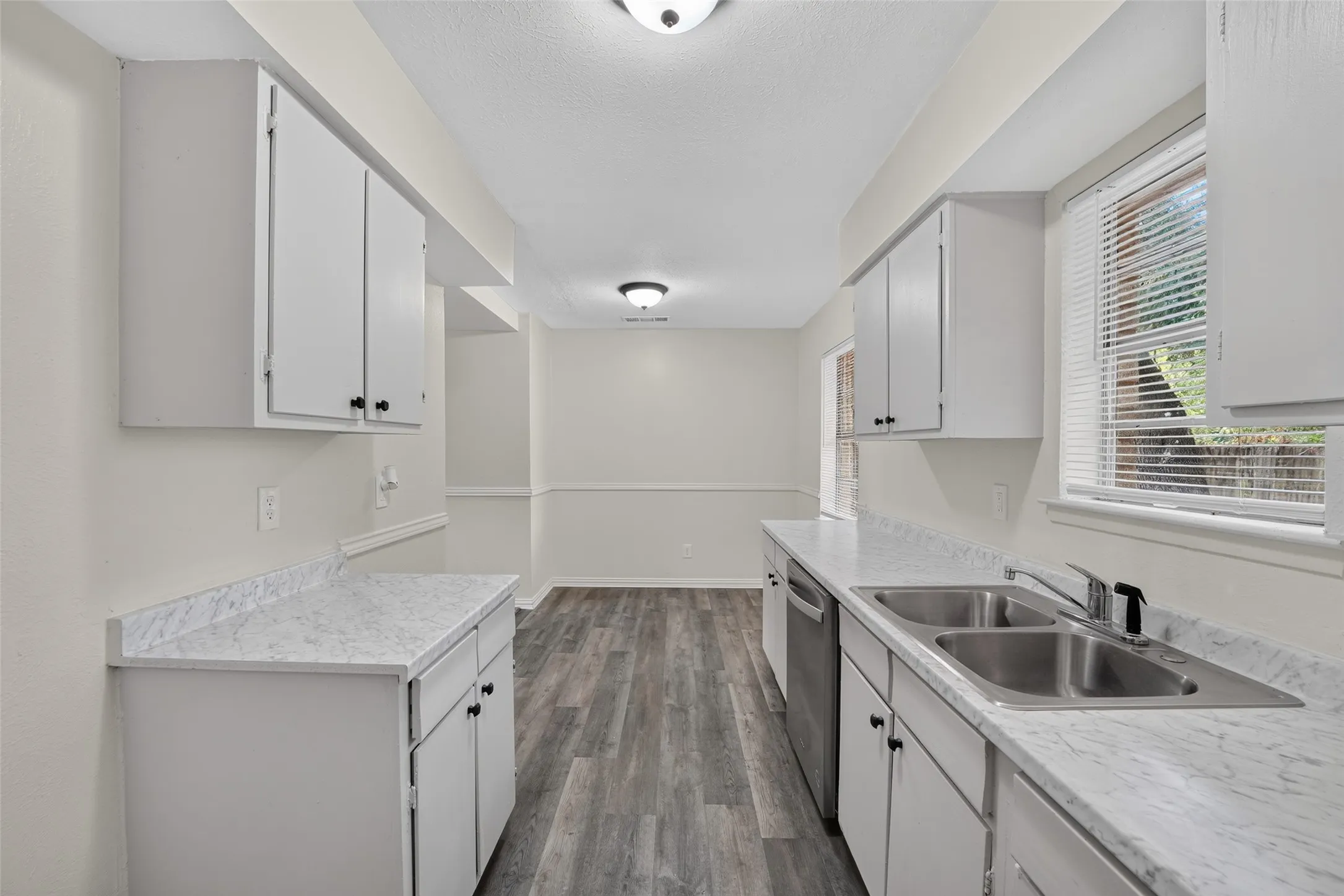 White cabinetry, dual basin stainless steel sink, stainless steel dishwasher, light-toned countertops, and wood-finish flooring