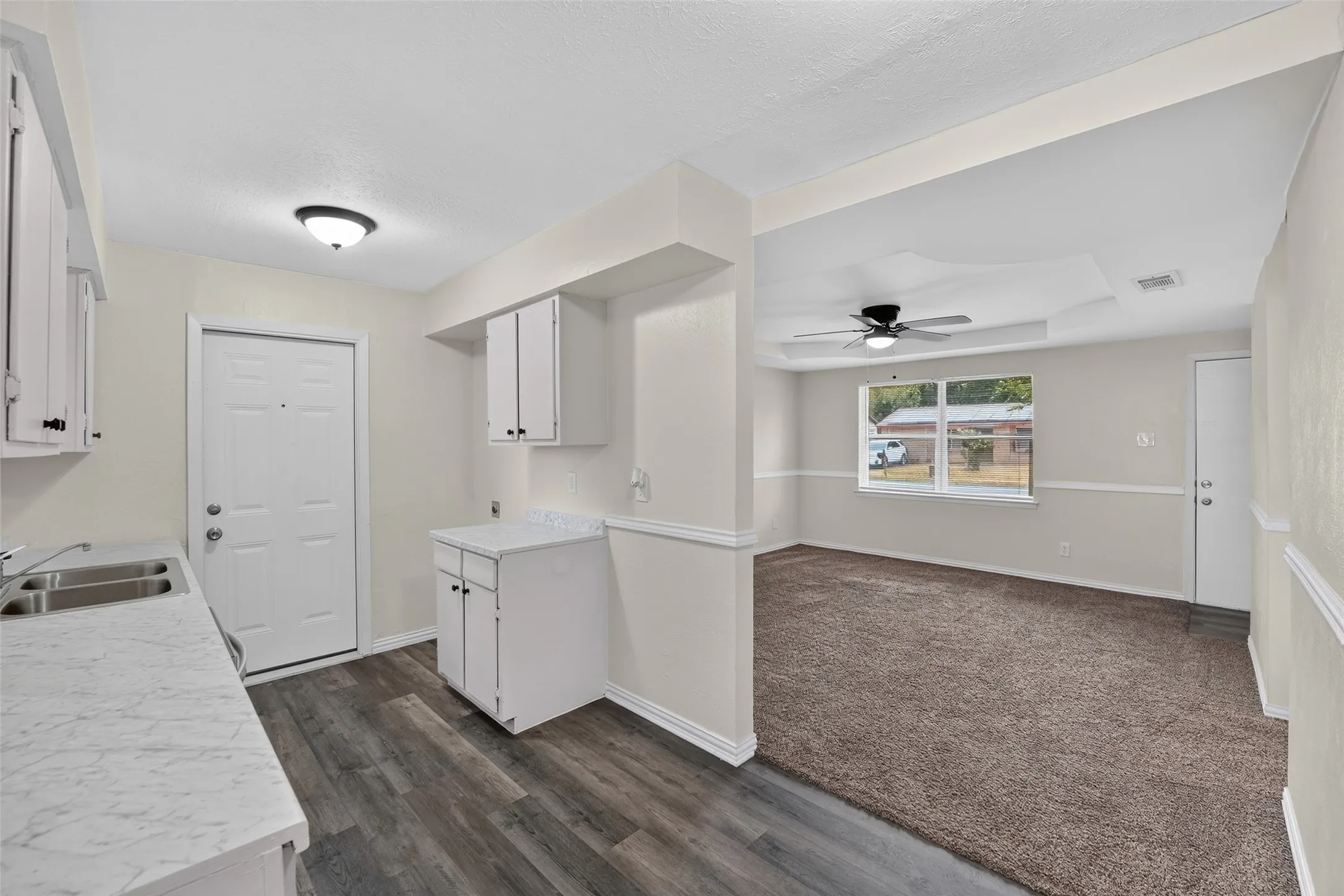 Wood-finish flooring, white cabinetry, double basin sink, tray ceiling, and ceiling fan