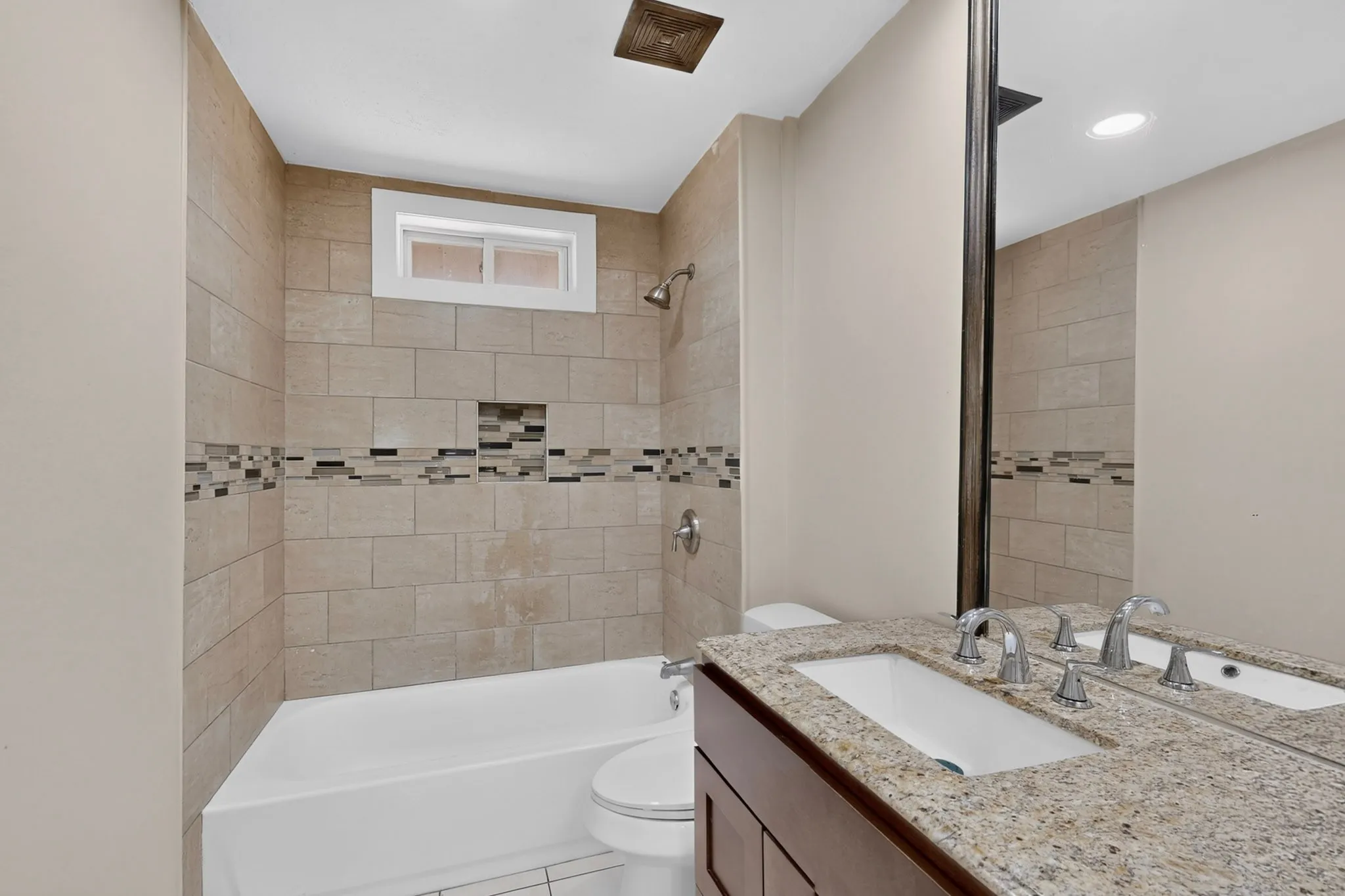 Bathtub with tiled surround, decorative mosaic accent, and integrated shower niche