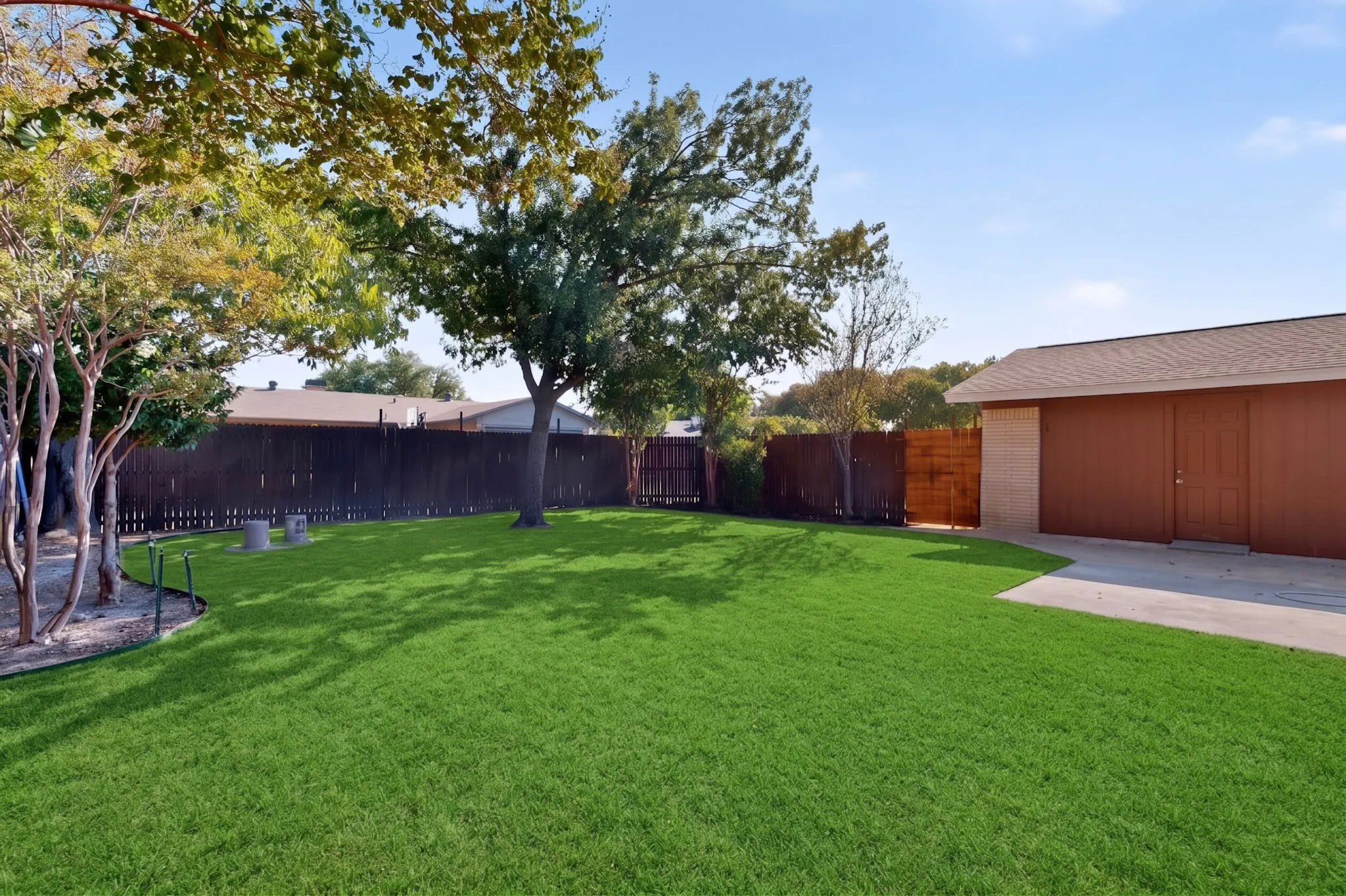 Expansive green lawn, mature trees, wood fence enclosure, and concrete patio