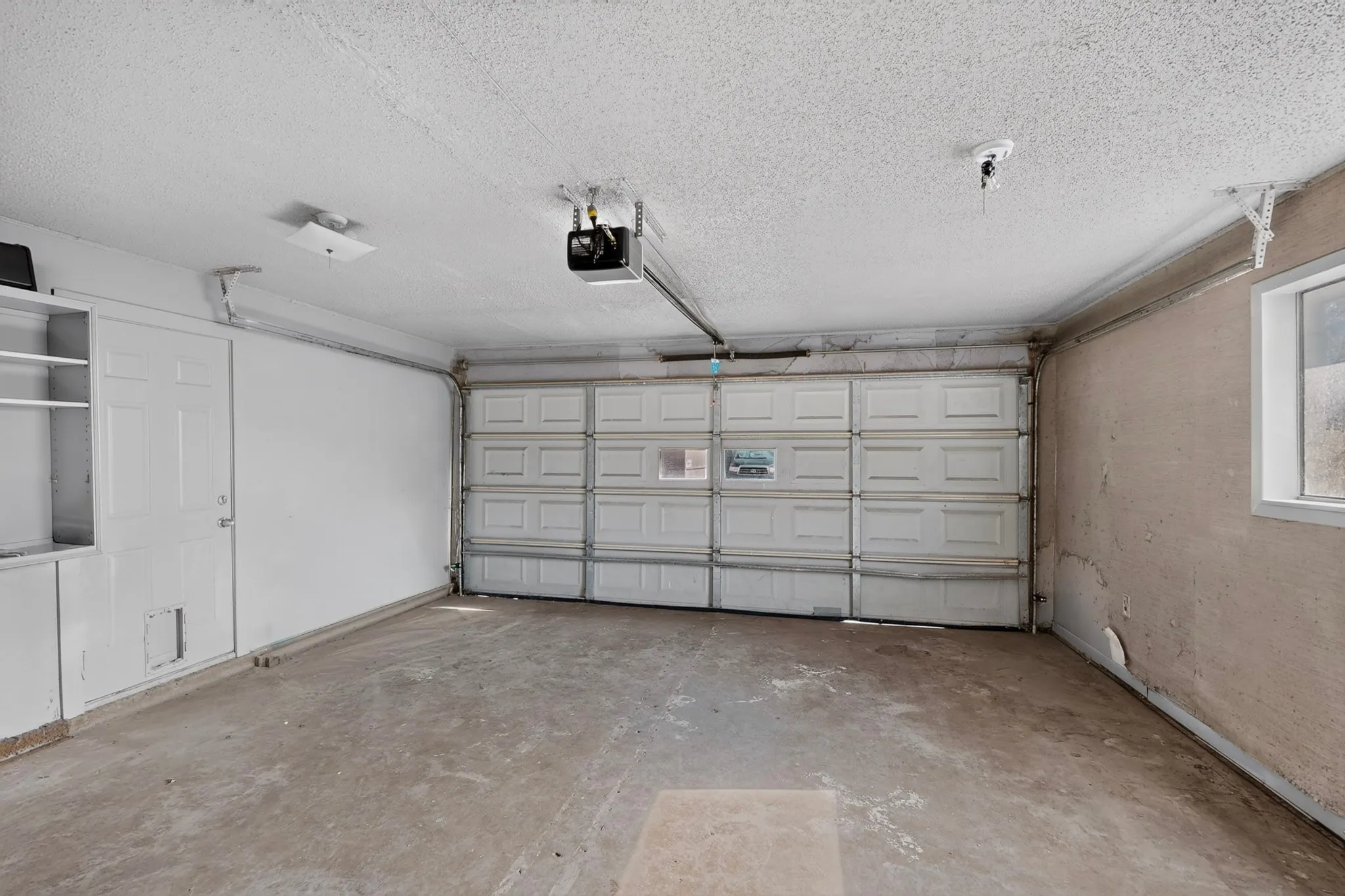 Attached garage featuring a concrete floor, built-in shelving, and garage door opener