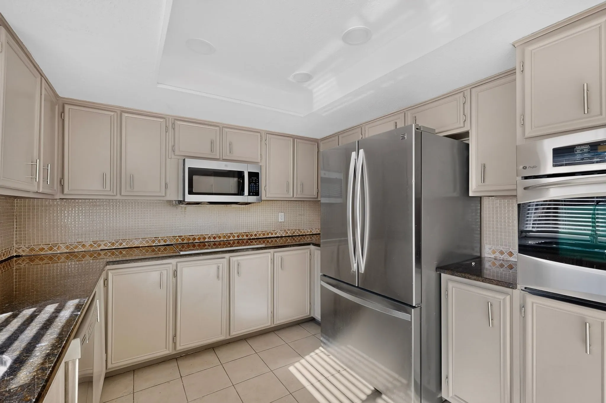 Stainless steel refrigerator, integrated microwave, built-in oven, extensive cabinetry, and tiled flooring