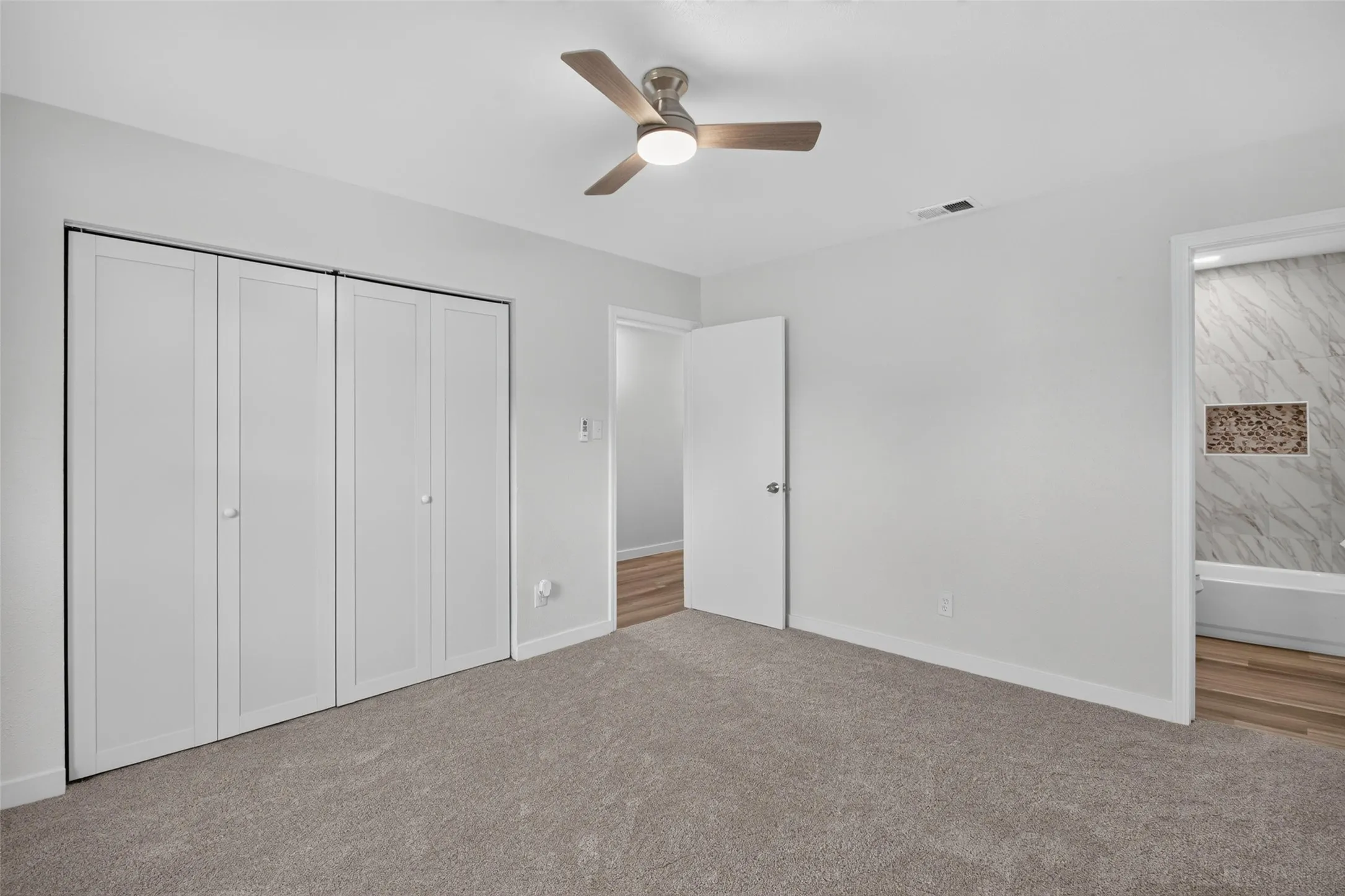 Neutral-toned carpeting, ceiling fan with light fixture, and bi-fold closet doors