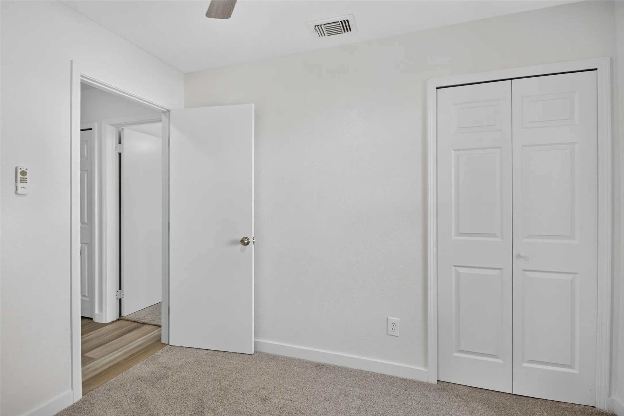 Neutral wall color, gray carpet, paneled bifold closet doors, white interior door, ceiling fan