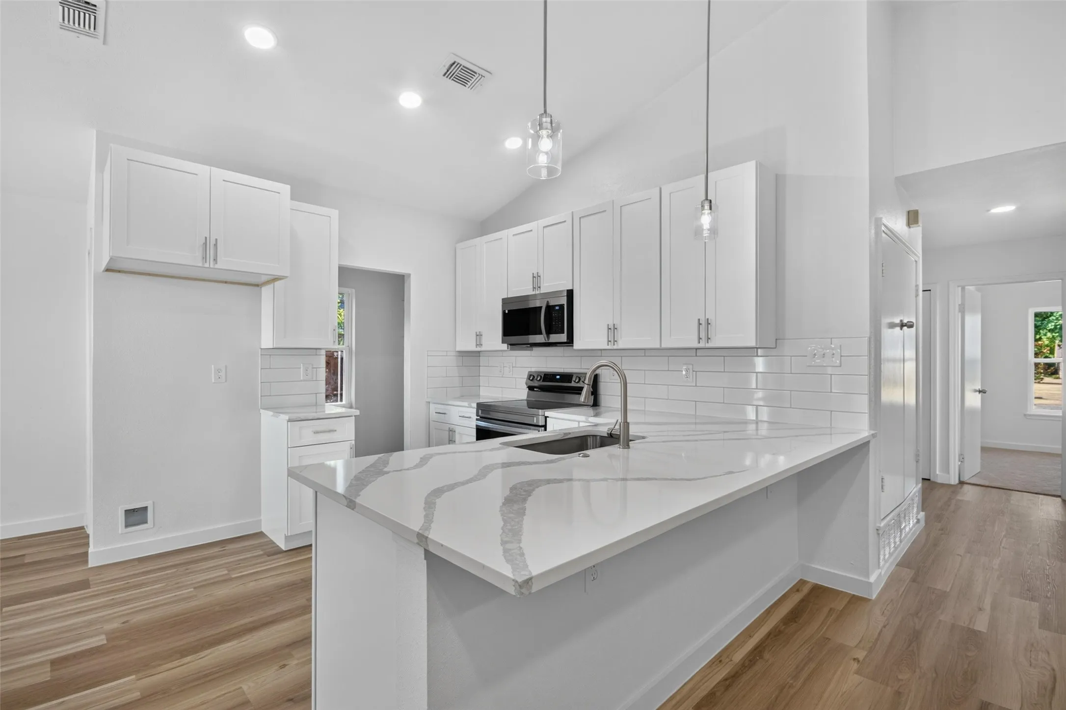 Modern kitchen featuring white shaker cabinetry, patterned countertops, stainless steel appliances, a subway tile backsplash, and wood-finish flooring