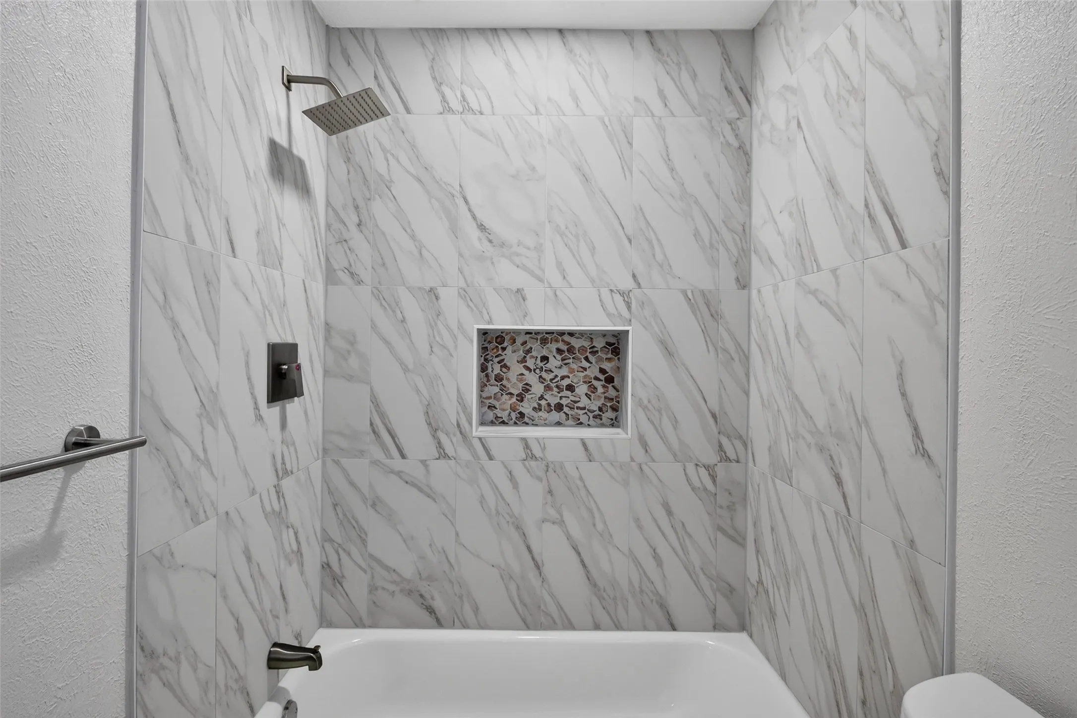 Bathtub with marble-patterned tile surround, built-in tile niche, and matte black shower fixtures