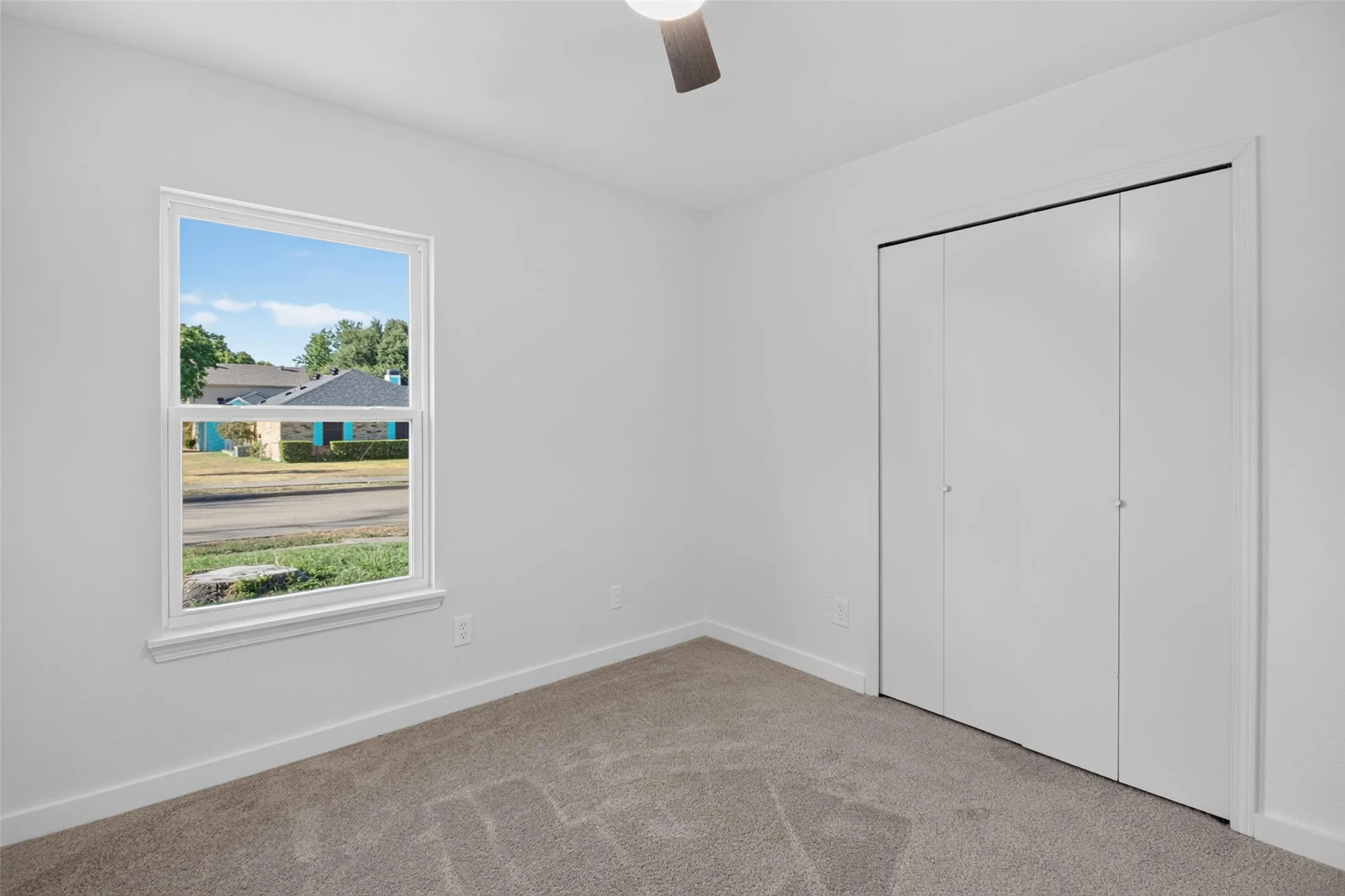 Light-colored carpeting, white walls, double-pane window, and a ceiling fan