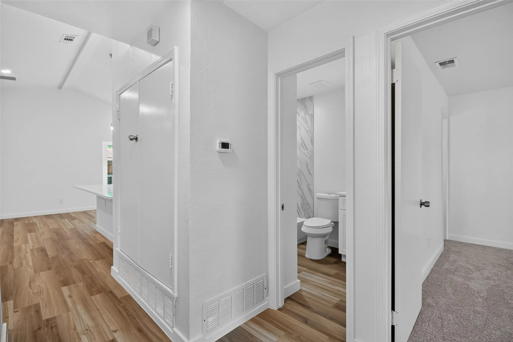 Modern hallway featuring white drywall construction, wood-finish flooring, recessed ceiling lighting, and direct access to a full bathroom with ceramic tile flooring and white cabinetry