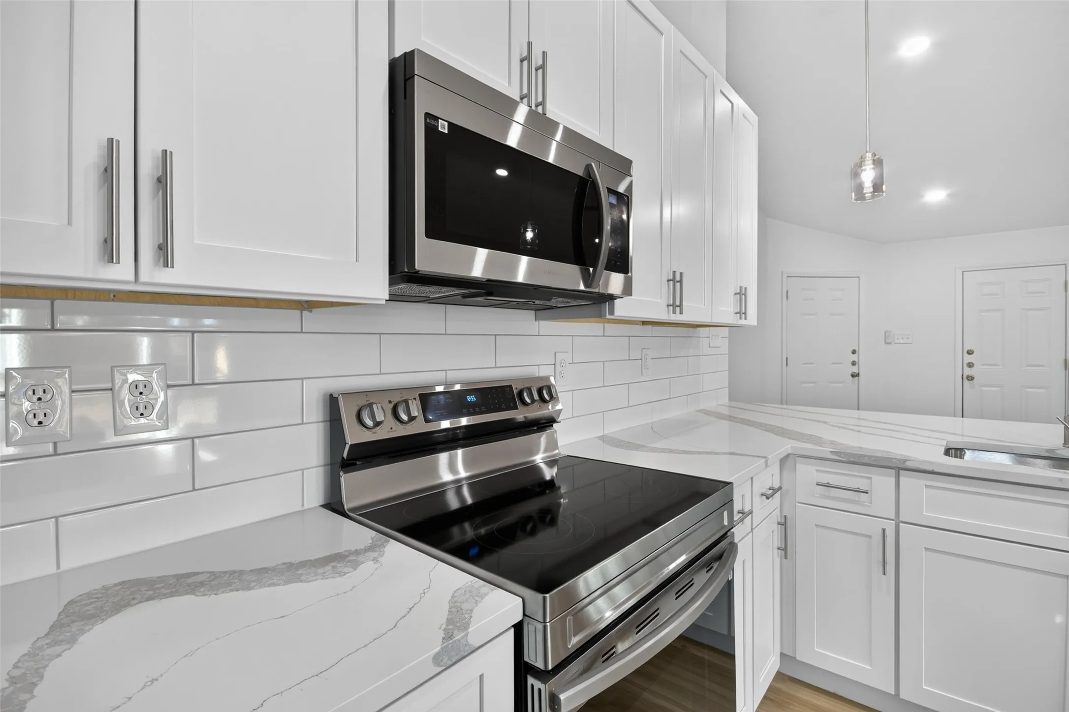 White shaker cabinetry, stainless steel appliances, white subway tile backsplash, and patterned countertops