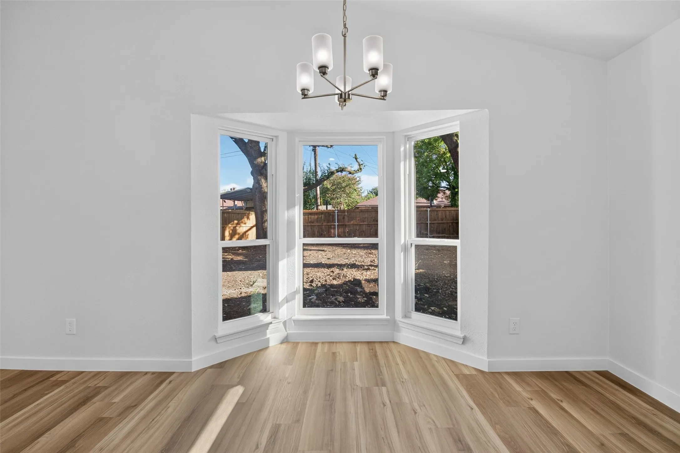Vaulted ceiling, modern chandelier, bay windows, wood-finish flooring, and white walls