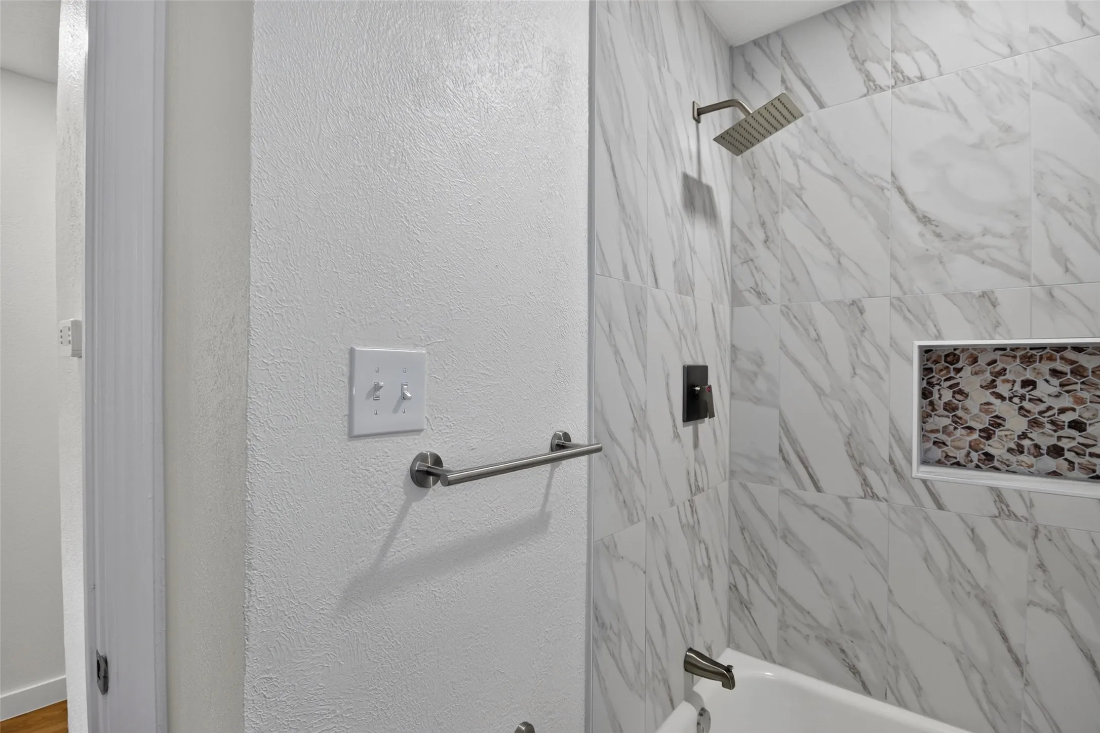 Tub-shower combination featuring large format tiled walls, a rain shower head, and a built-in niche with pebble tile accent