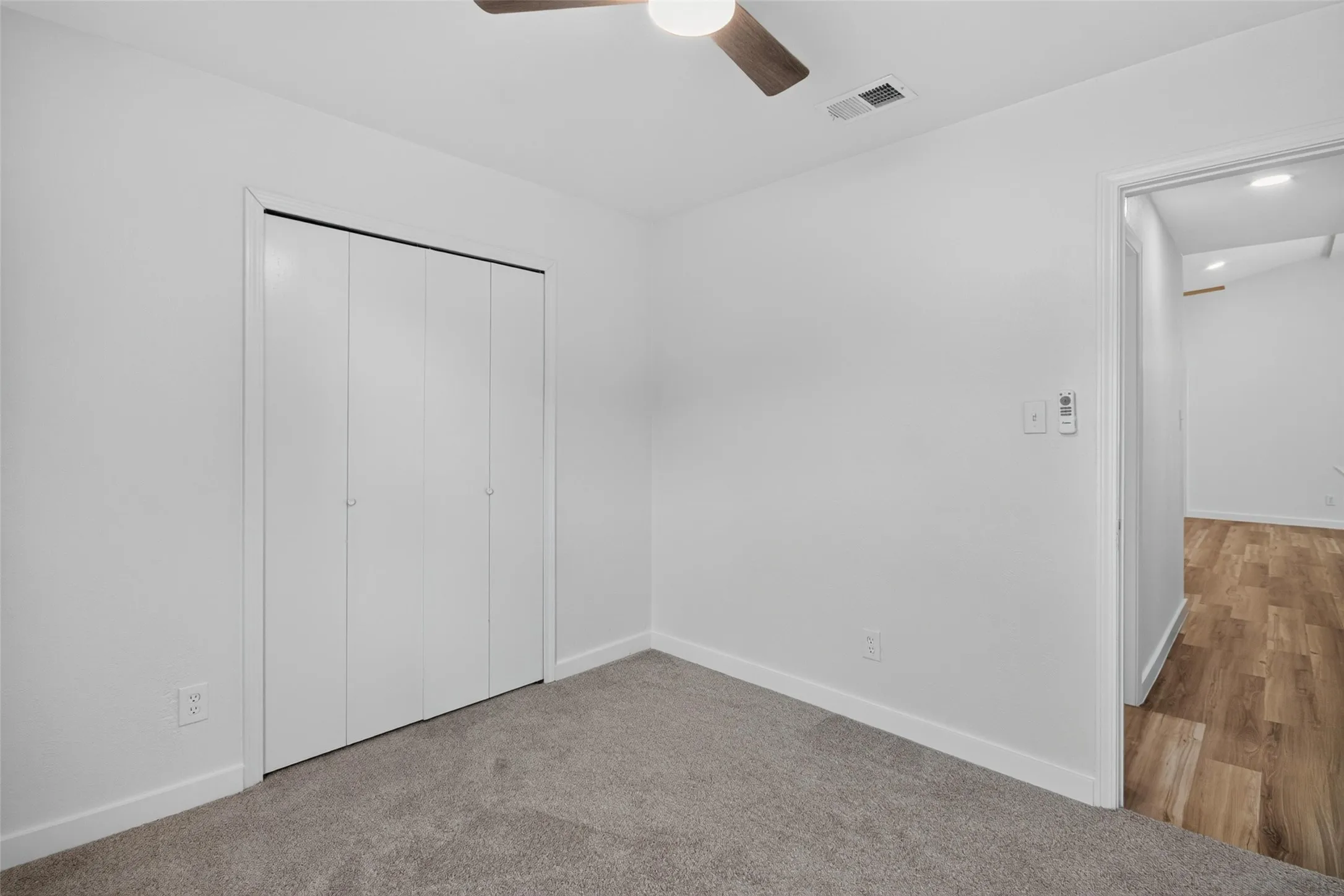 Neutral wall paint, carpet flooring, bi-fold closet doors, ceiling fan, wood-finish flooring visible through doorway