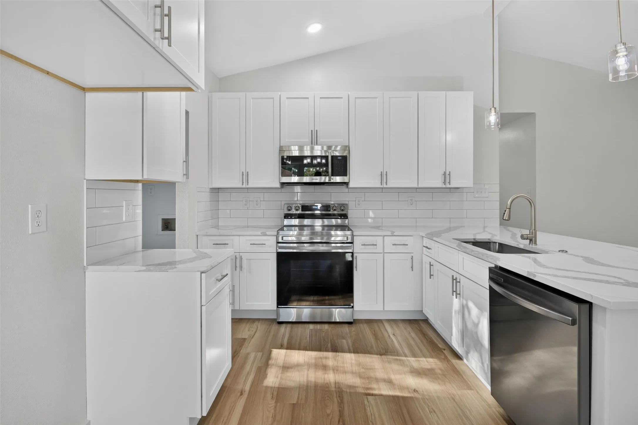Vaulted ceilings, wood-finish flooring, white cabinetry, stainless steel appliances, and a subway tile backsplash