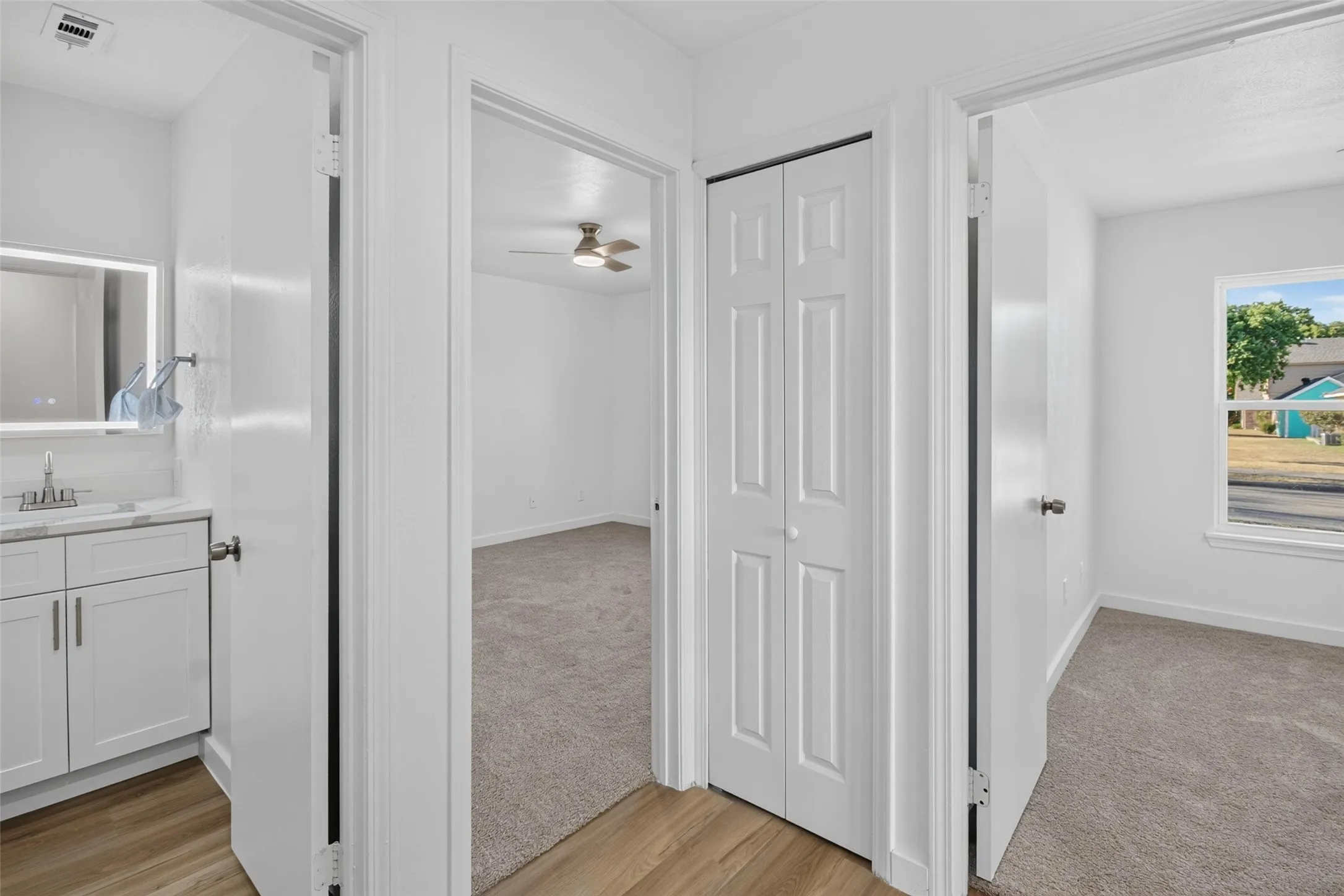 Vanity with white cabinetry and countertop, illuminated mirror, wood-finish flooring, carpeted rooms, ceiling fan